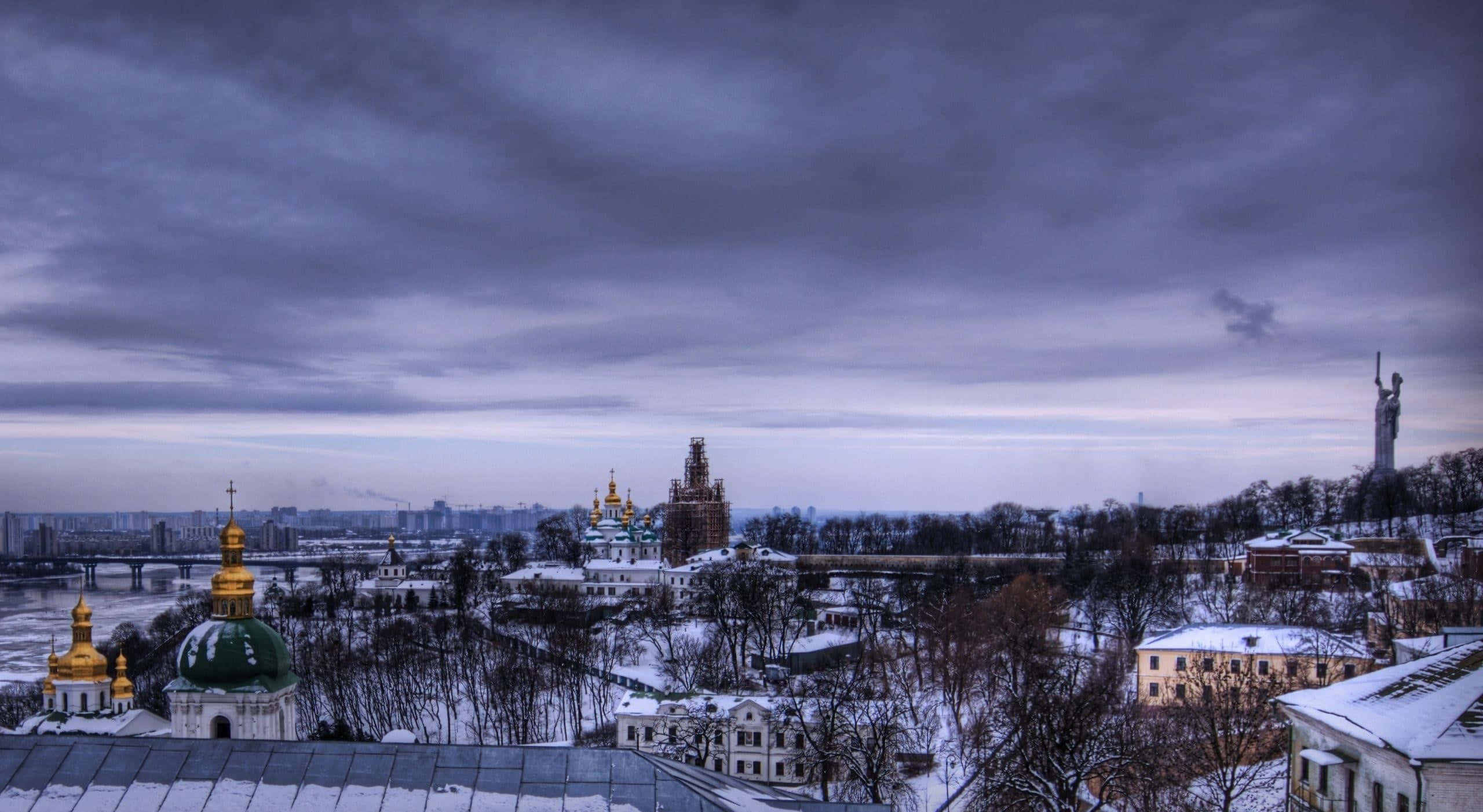 Winter Cityscape 桌布 壁紙 — 白雪覆蓋歷史悠久的教堂和建築，在冬日城市景觀中，暮色蒼茫的天空下。
