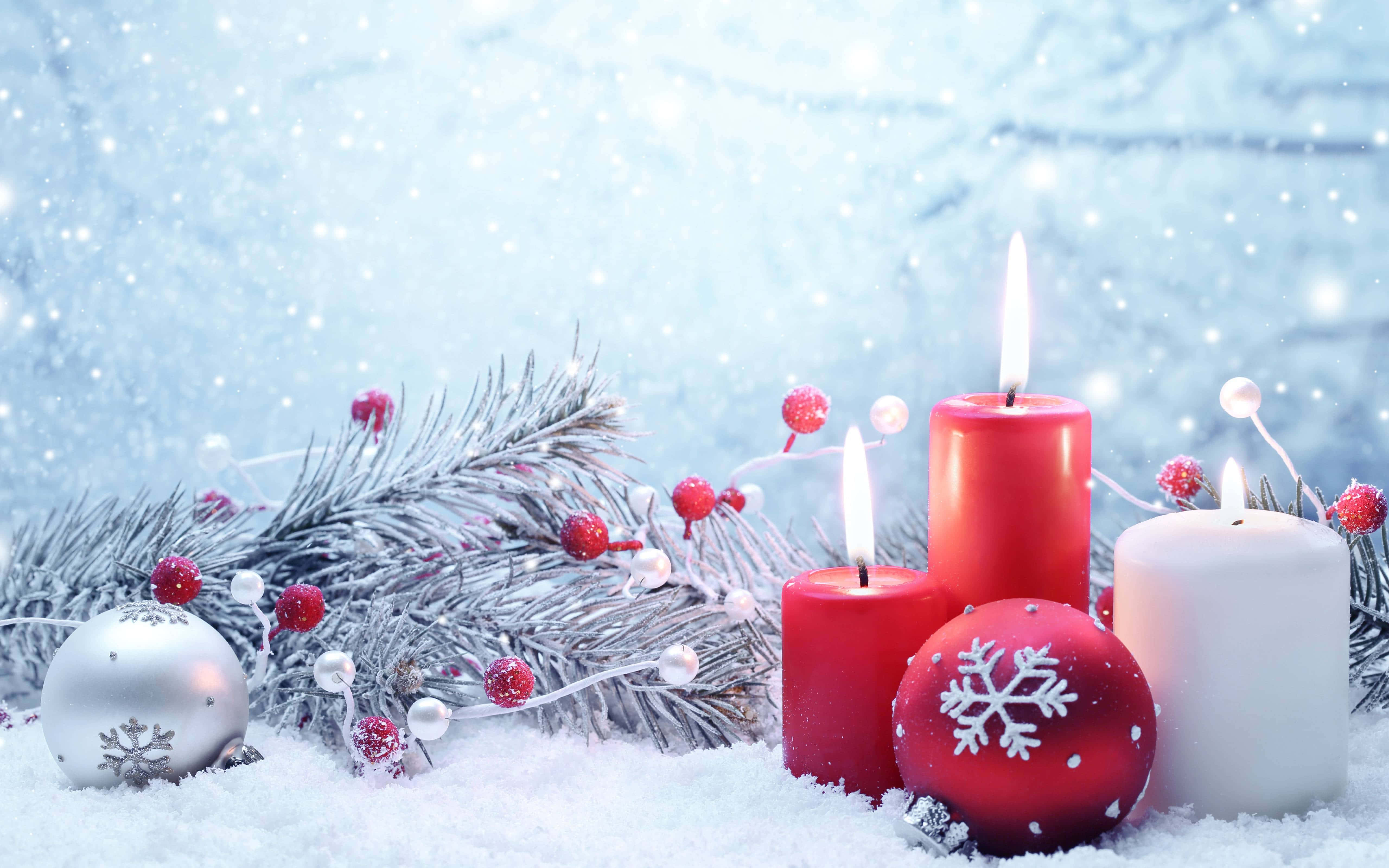 Snowy Christmas 桌布 壁紙 — 白雪覆蓋的冬日場景，紅色和白色的蠟燭在結霜的松樹枝和節日裝飾旁閃耀。