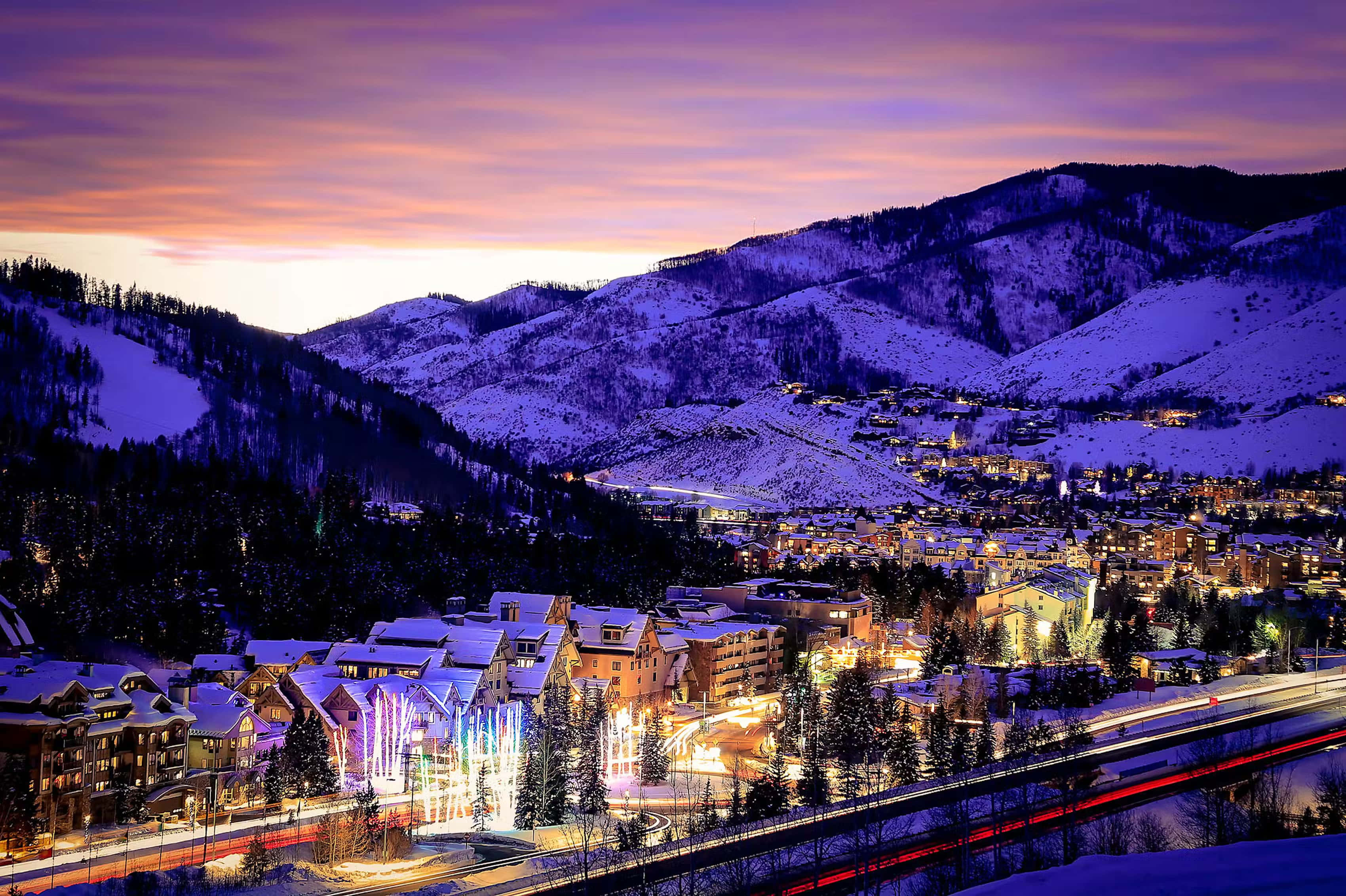 Colorado 桌布 壁紙 — 白雪覆蓋的山城在充滿活力的紫色和橙色暮色天空下閃耀著溫暖的燈光。