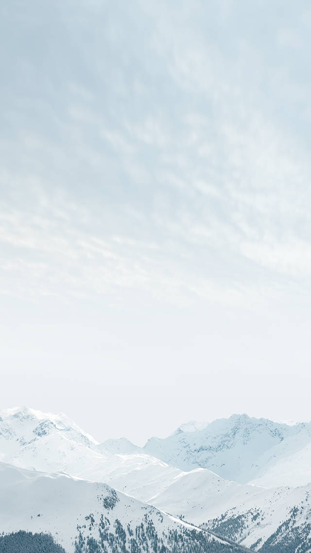 冬天 桌布 壁紙 — 白雪覆蓋的山峰在柔和淡藍色的天空下升起，伴隨著縷縷雲彩。