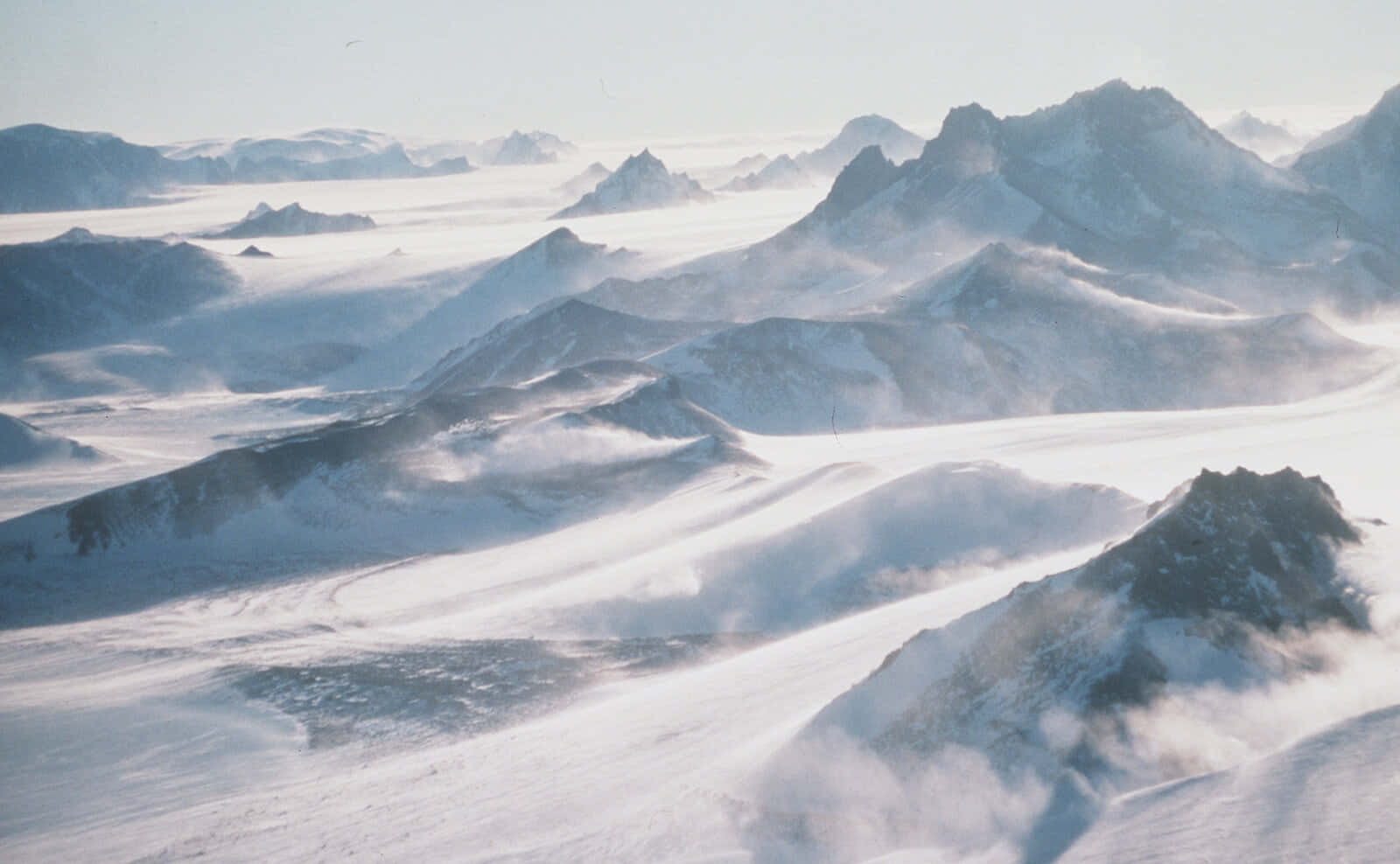 Antarctica 桌布 壁紙 — 白雪覆蓋的山峰在蒼白的天空下，穿過旋轉的迷霧，矗立在廣闊的阿爾卑斯山區。