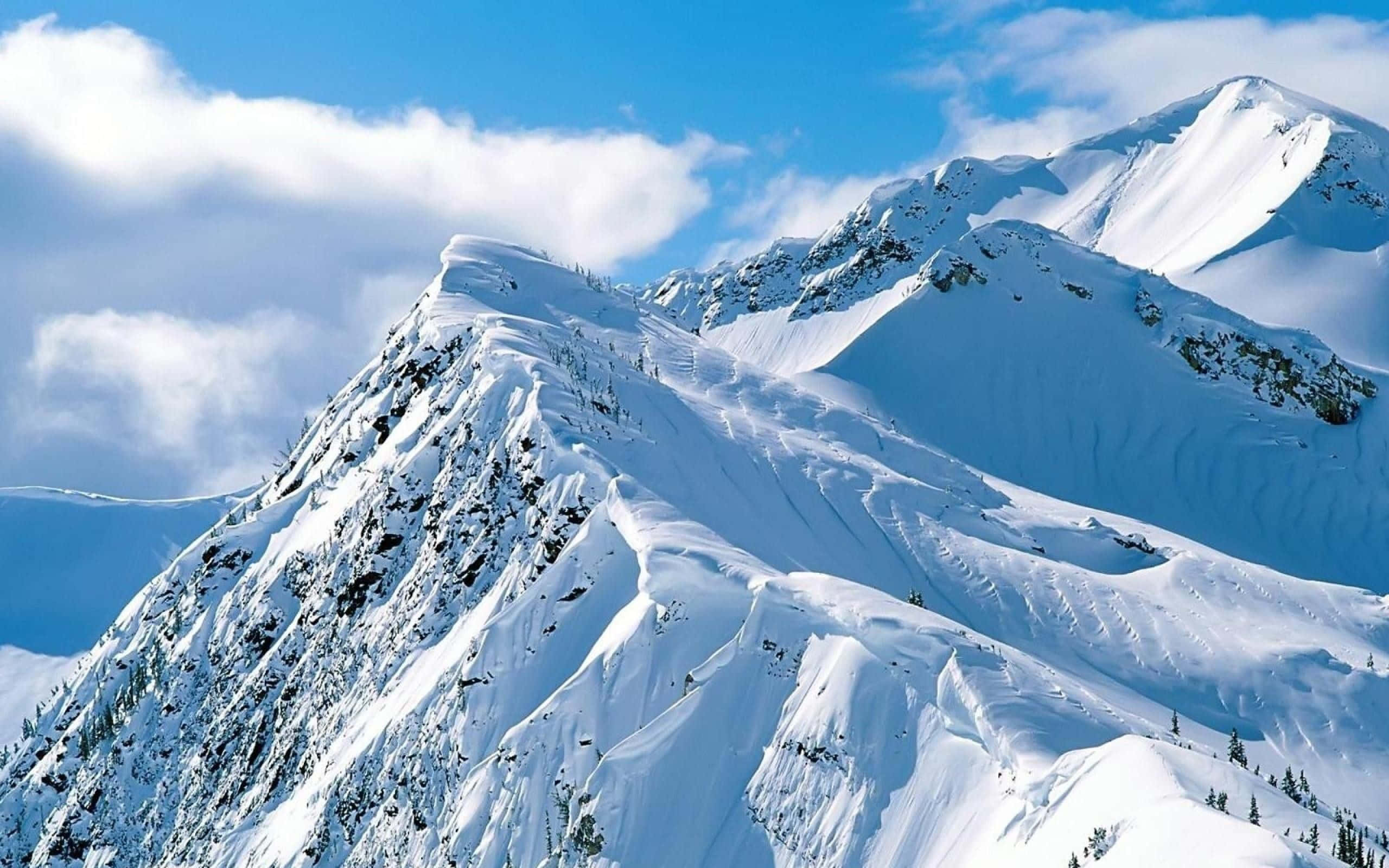 Snowy Landscape 桌布 壁紙 — 白雪覆蓋的山峰在藍天白雲下巍然聳立。