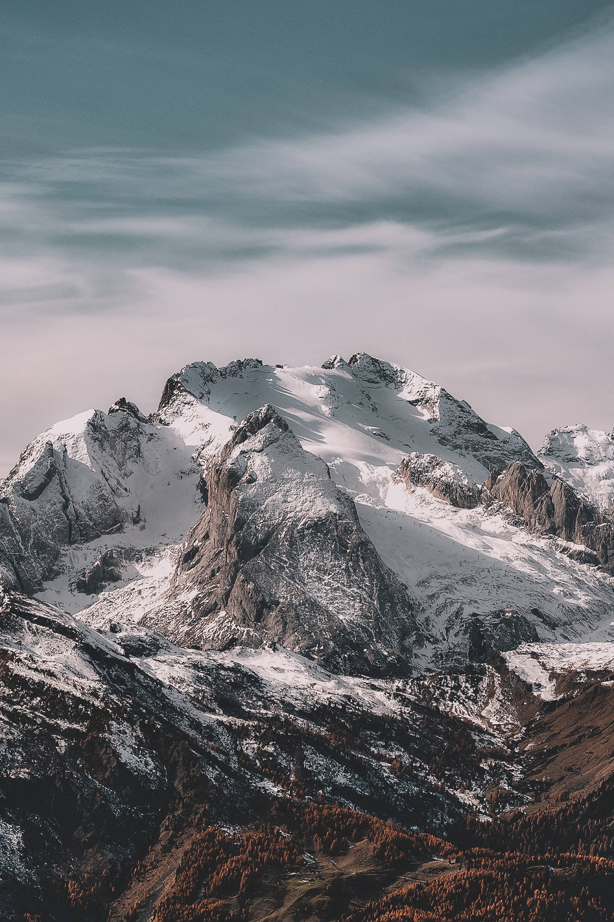 Mountain 桌布 壁紙 — 白雪覆蓋的山峰穿透柔軟多雲的天空，下方是秋日森林覆蓋的山坡。