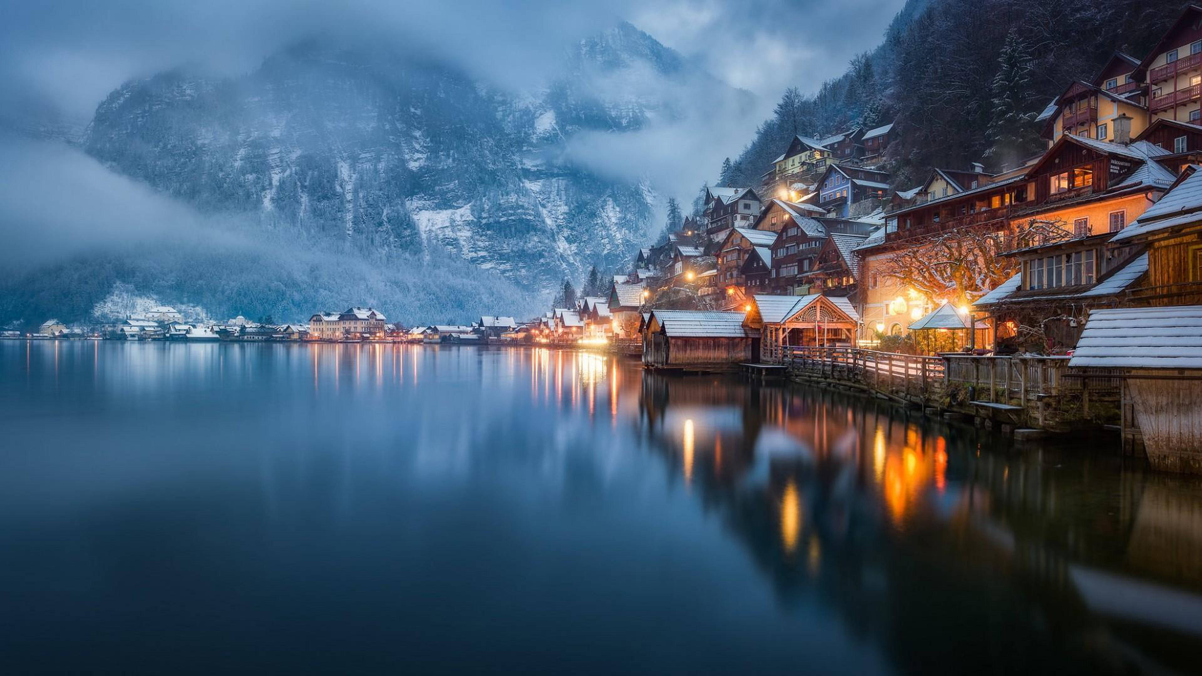 Norway 桌布 壁紙 — 白雪覆蓋的山村燈光在薄霧暮色下溫暖地倒映在平靜的湖面上。