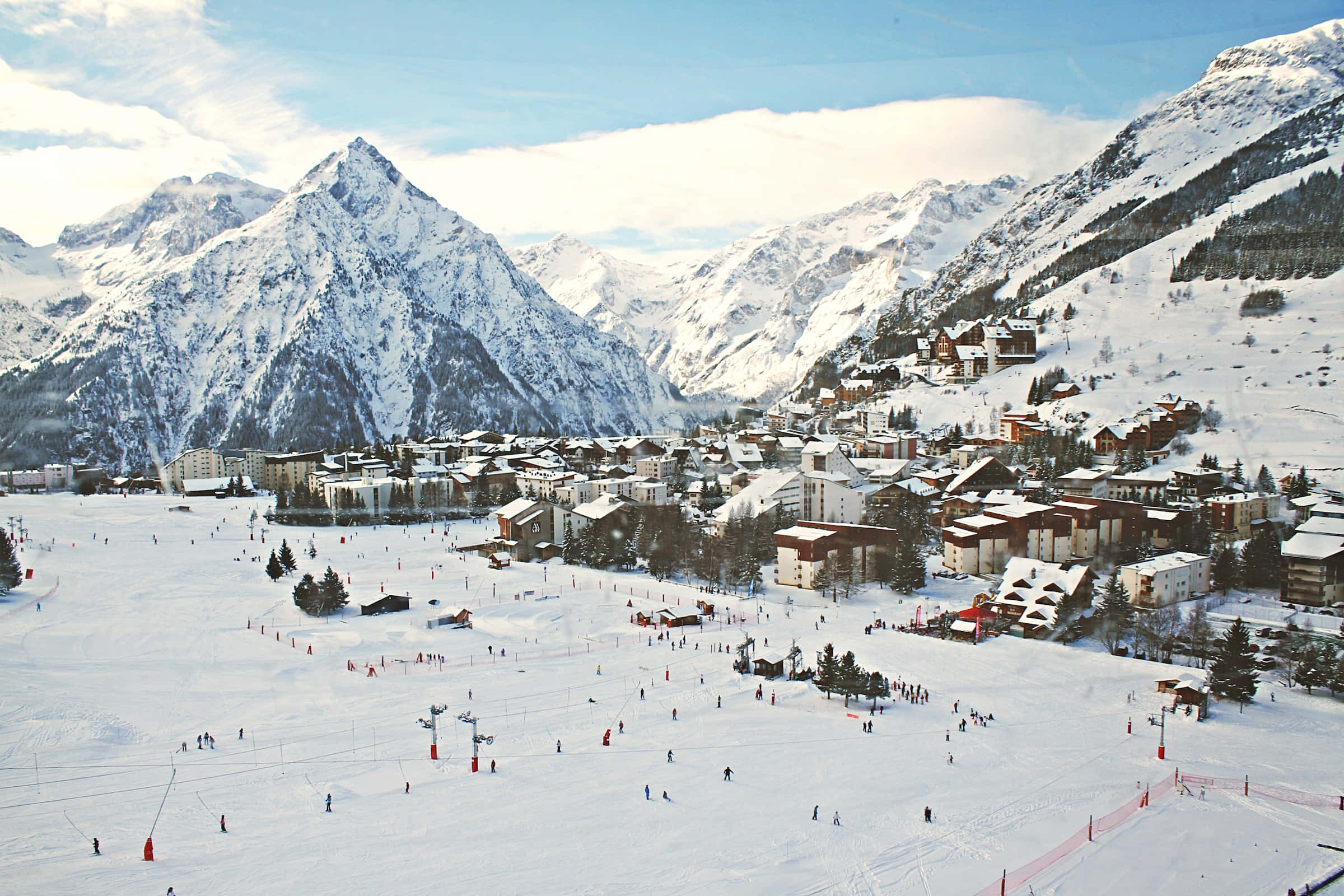 Ski Resort 桌布 壁紙 — 白雪覆蓋的山村鳥瞰圖，在明亮的藍天下滑雪者熙熙攘攘。
