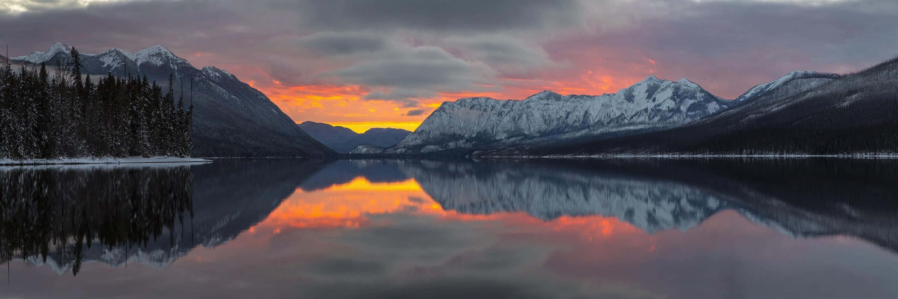 Sunset Reflection 桌布 壁紙 — 白雪覆蓋的山脈在橙紫色雲彩的熾熱日落中倒映在平靜的湖面上。