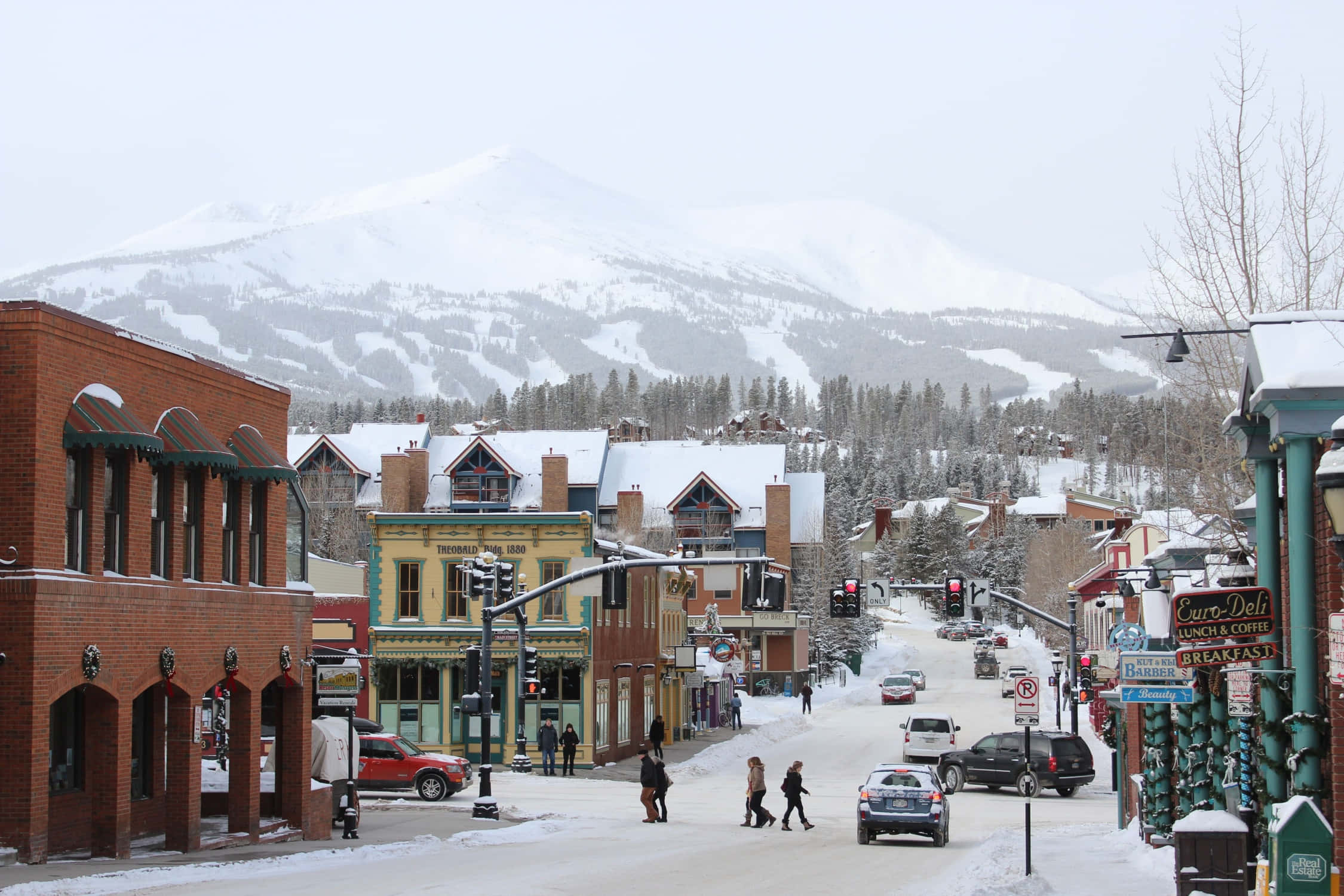 Colorado 桌布 壁紙 — 白雪覆蓋著一條古雅的山城街道，兩旁是歷史悠久的磚砌建築，遠方是白雪覆蓋的山峰，天空灰濛濛。