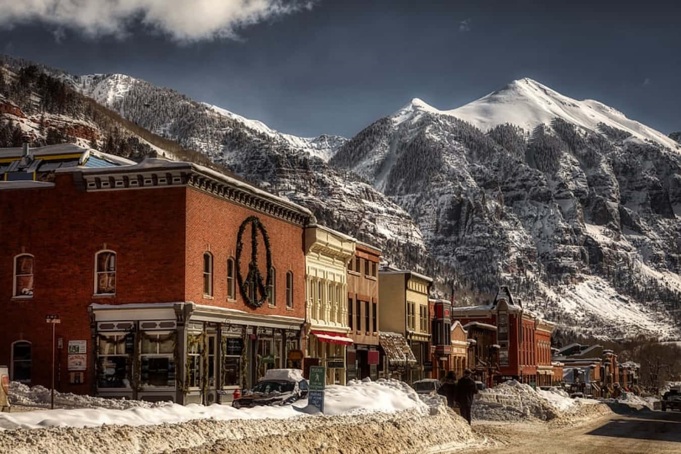 Colorado 桌布 壁紙 — 白雪覆蓋著一條古雅的山城街道，兩旁是歷史悠久的磚砌建築，上方是戲劇性的多雲天空。