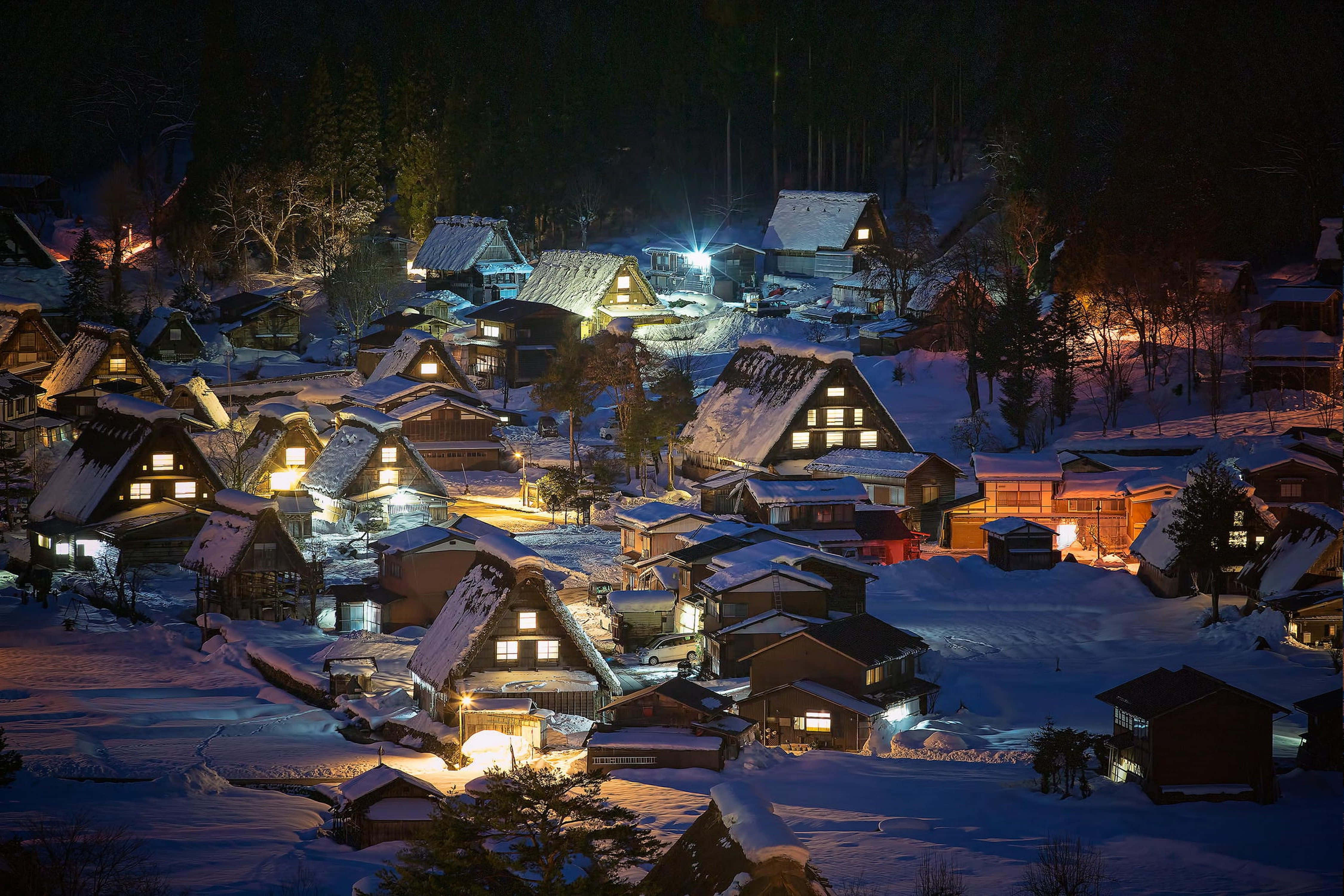Snowy Village 桌布 壁紙 — 白雪覆蓋著傳統的日本村莊房屋，在夜空下溫暖地發光。