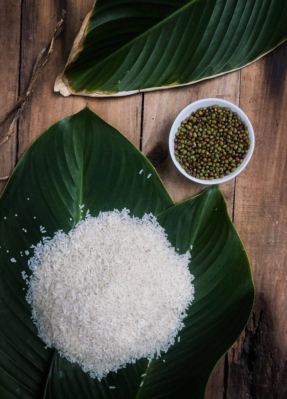 白飯與綠葉及黃豆碗 壁紙 — 白米和綠豆放在大綠葉上，置於質樸的木質表面上。