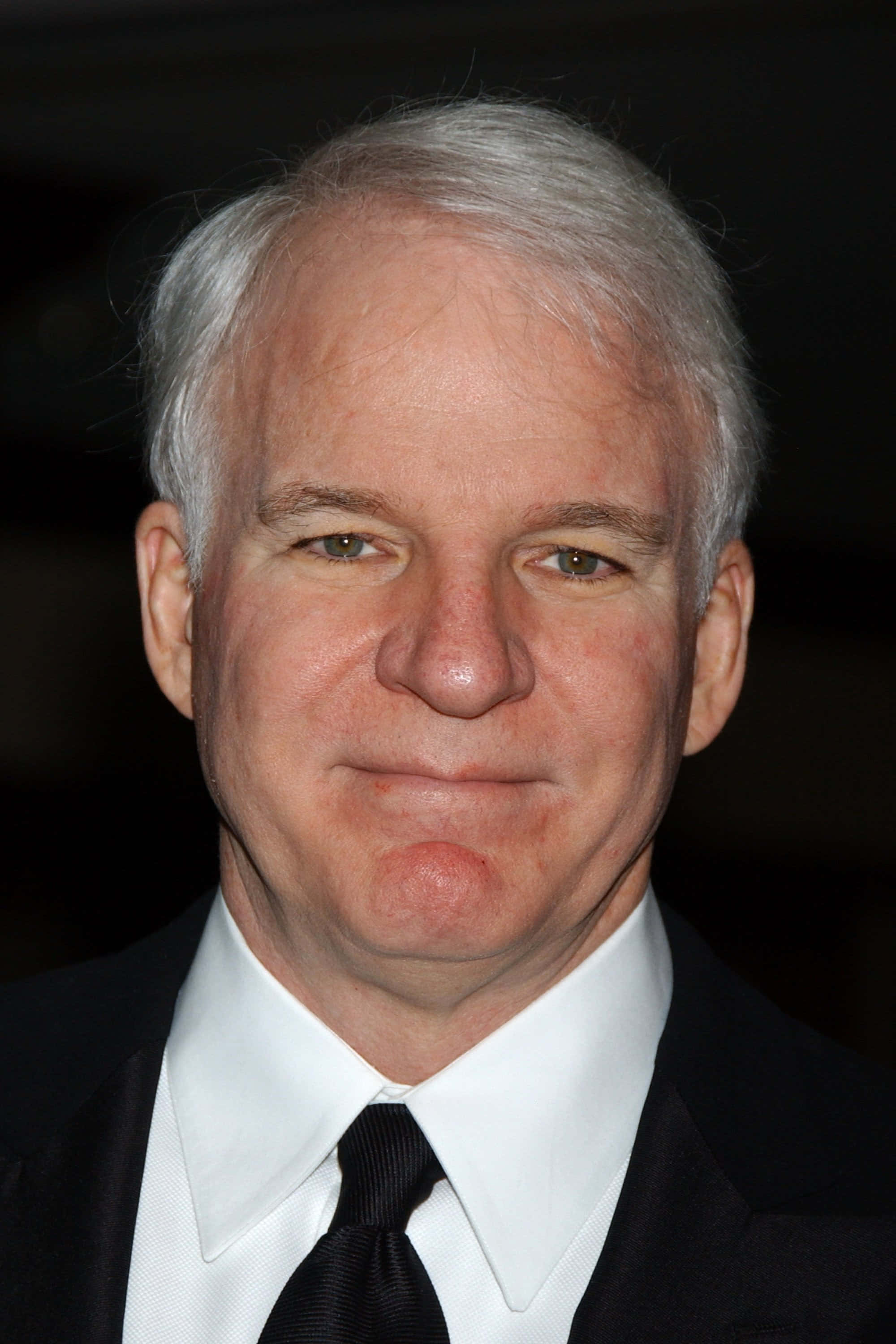 steve martin 桌布 壁紙 — 白髮男子身穿黑色西裝打領帶，在深色背景前的特寫肖像。