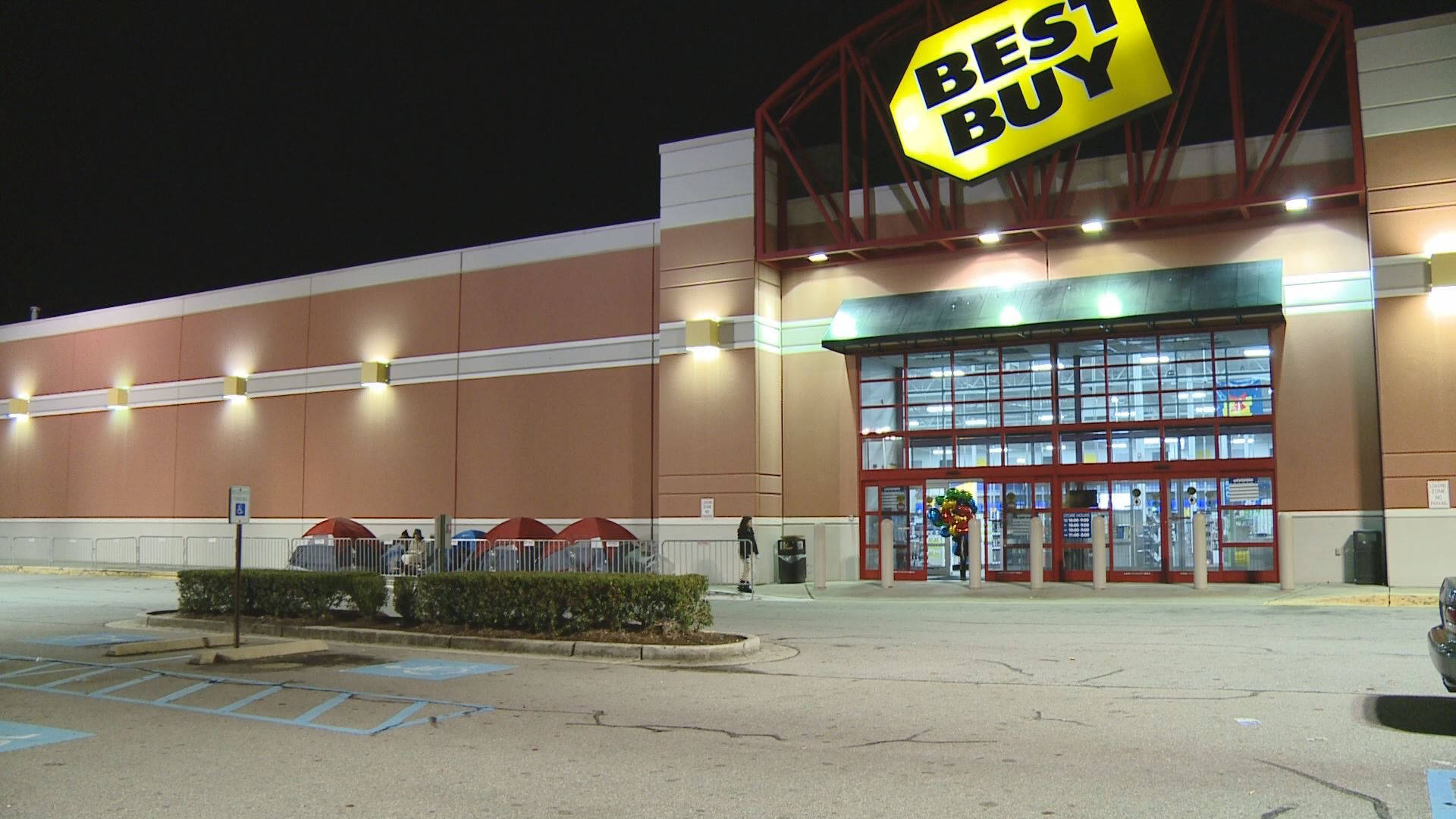 百思 buy 夜間外觀 壁紙 — 夜晚燈火通明的Best Buy商店，發光的標誌和入口附近的人們。