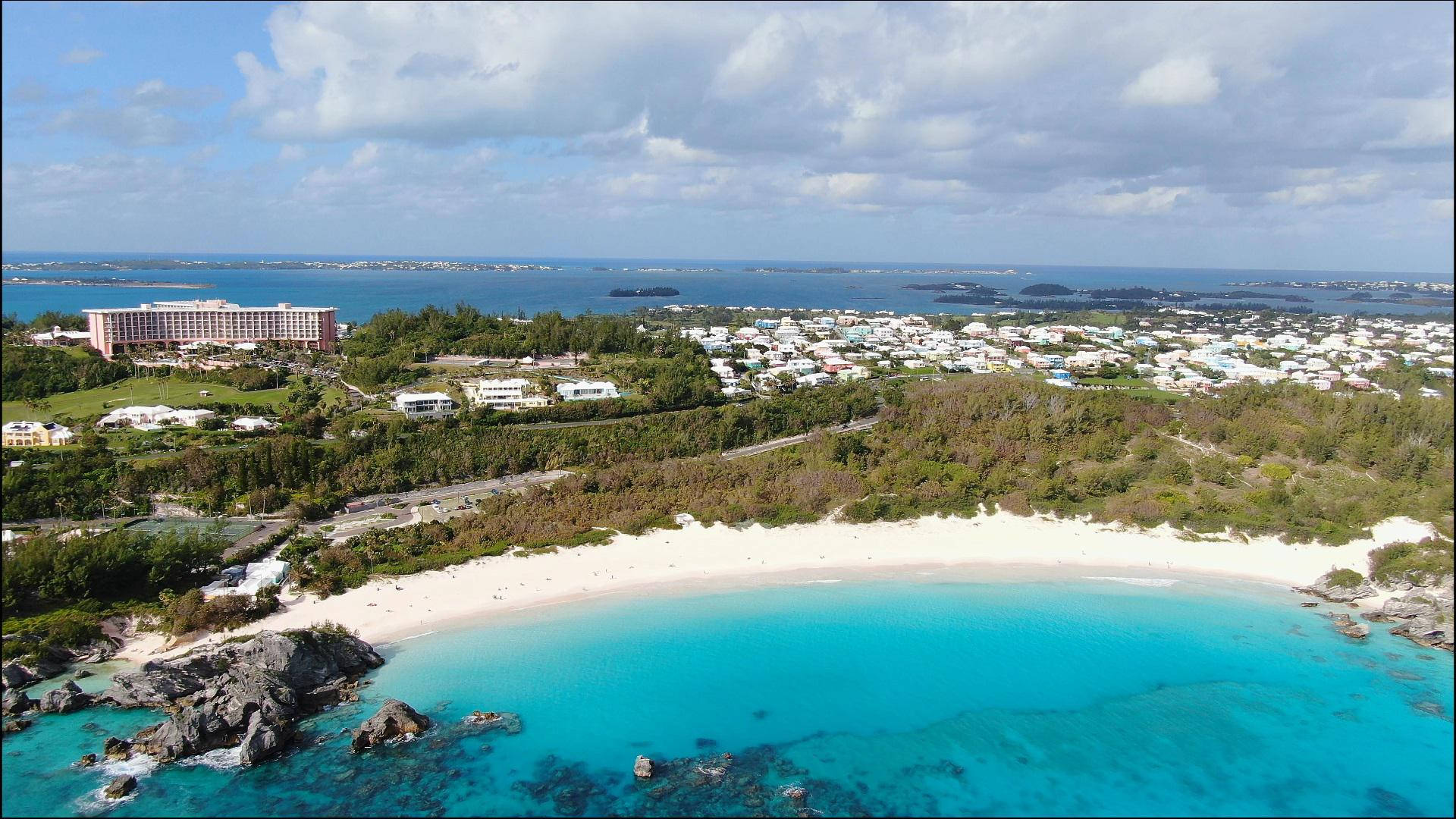 新月形海灘，藍綠色海水，度假村建築隱藏在綠色山丘之間。