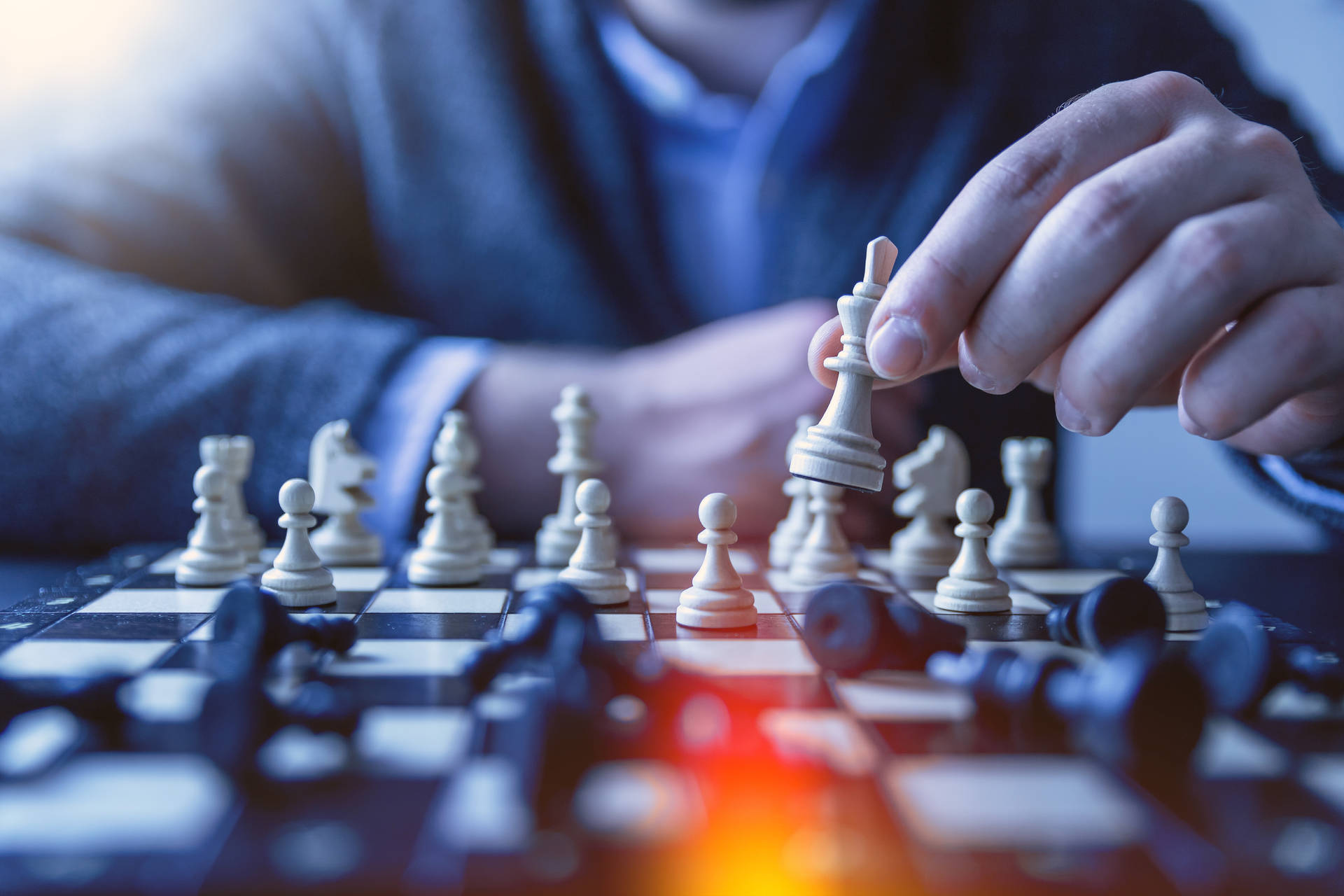手在棋盤上移動國際象棋王棋，棋盤上有倒下的棋子和溫暖的光暈。