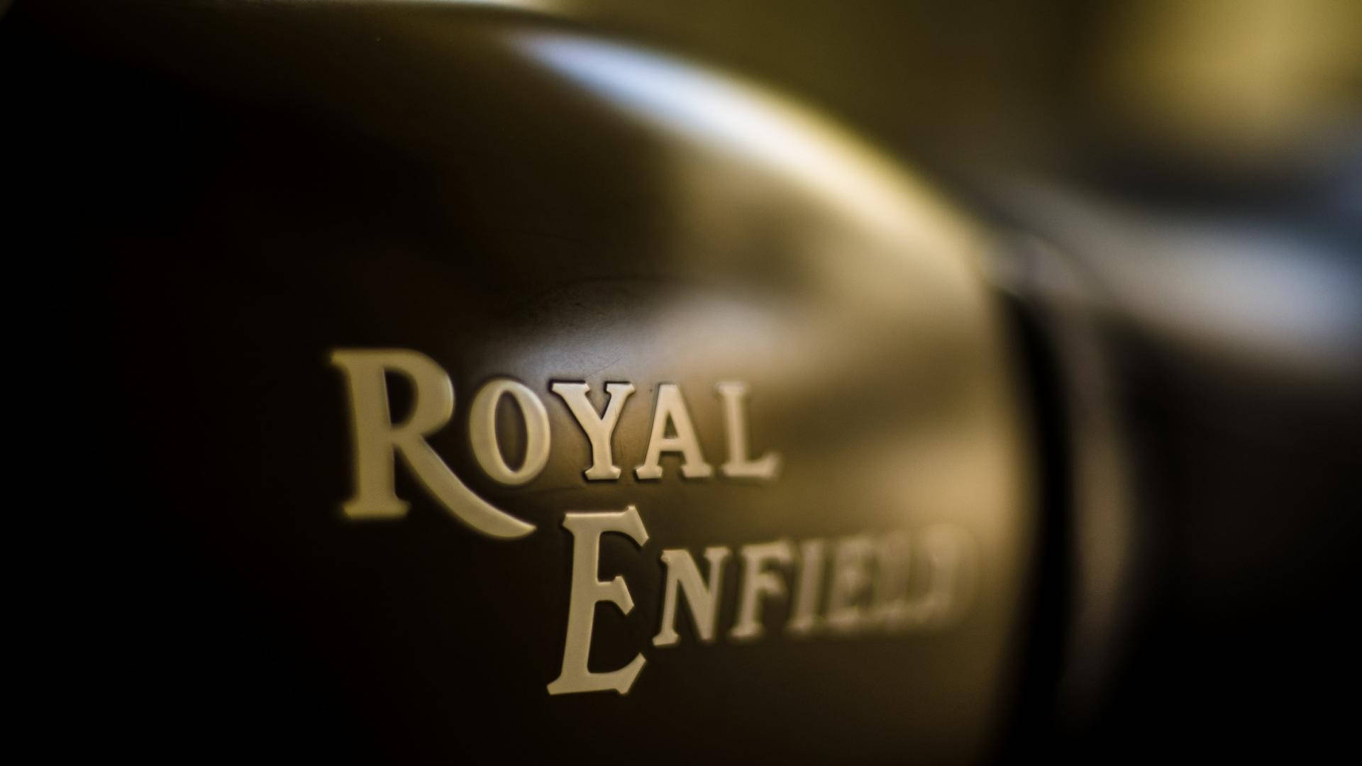 皇家恩菲德 HD 品牌名稱特寫 壁紙 — 金色Royal Enfield標誌特寫，壓印在時尚黑色電單車油箱上，配以柔和燈光。
