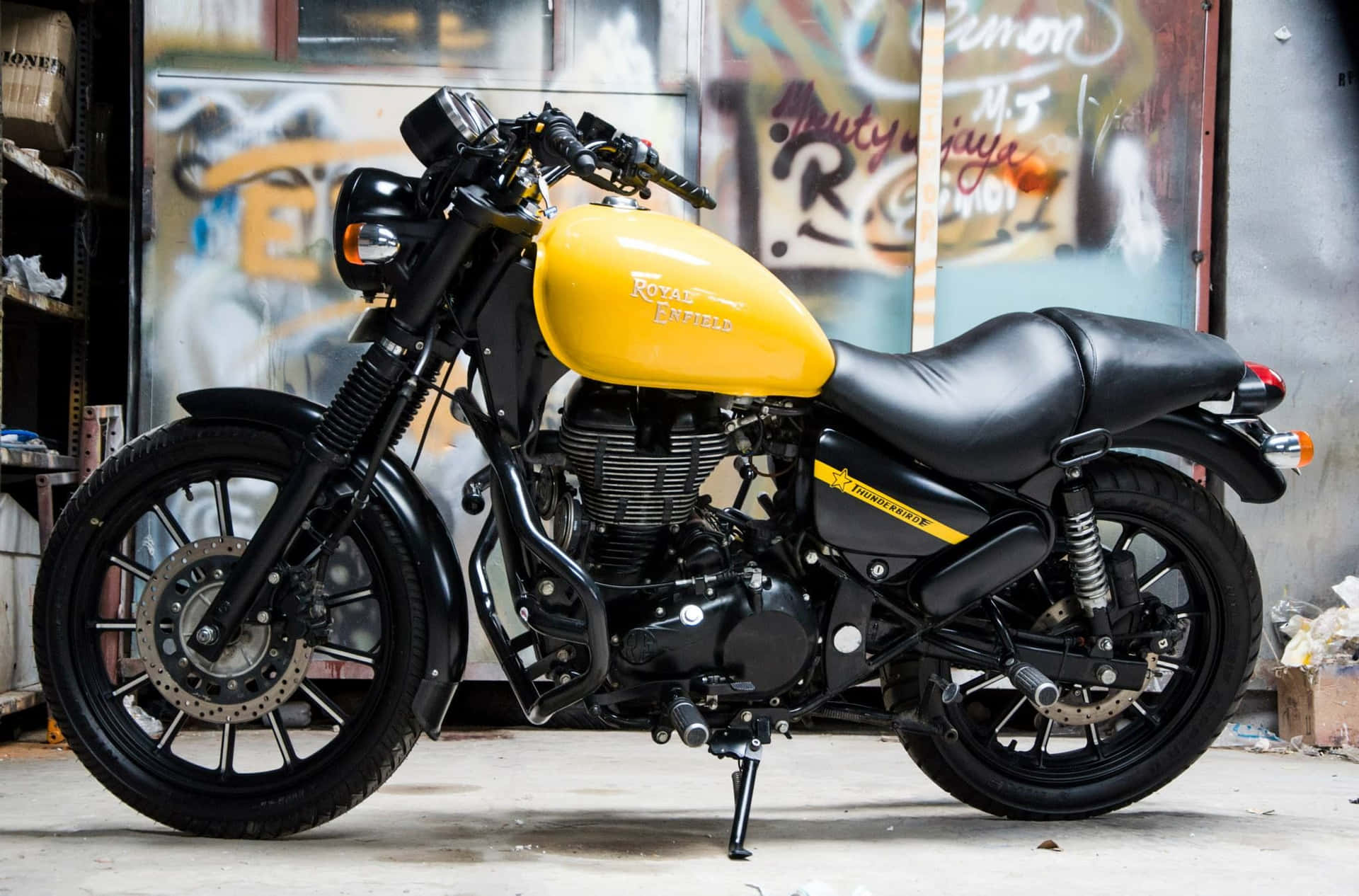 黃黑色 Royal Enfield 電單車停泊在佈滿塗鴉的車庫內。