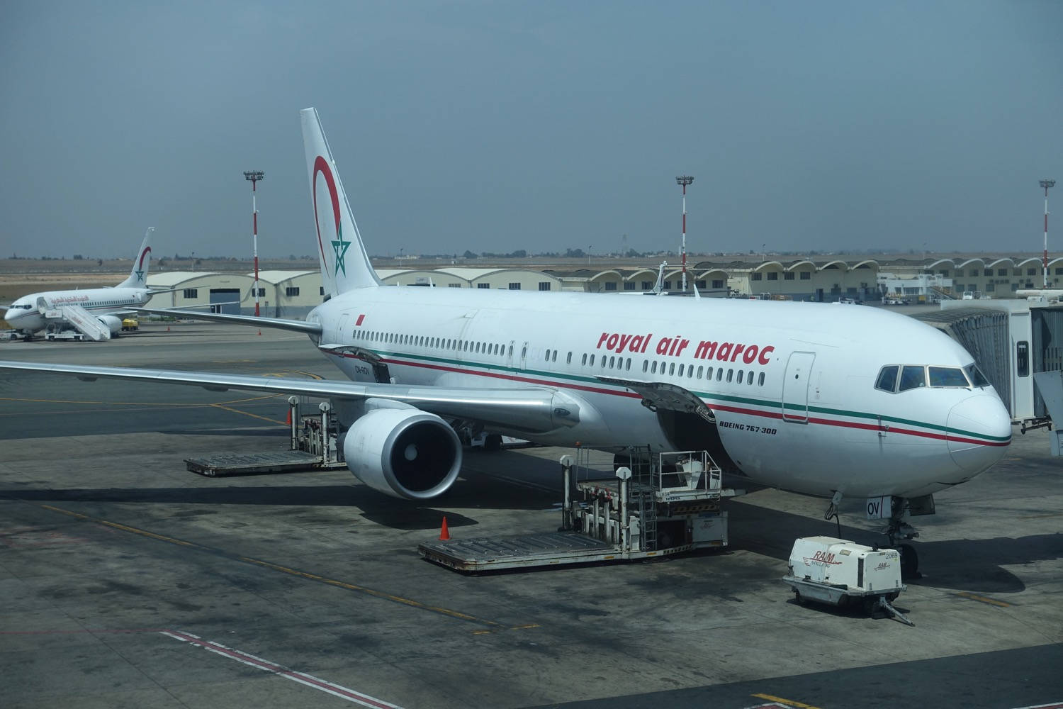 皇家摩洛哥航空貨運飛機與貨車 壁紙 — 一架皇家摩洛哥航空波音767停泊在機場閘口，地面服務設備和另一架飛機在背景中可見。