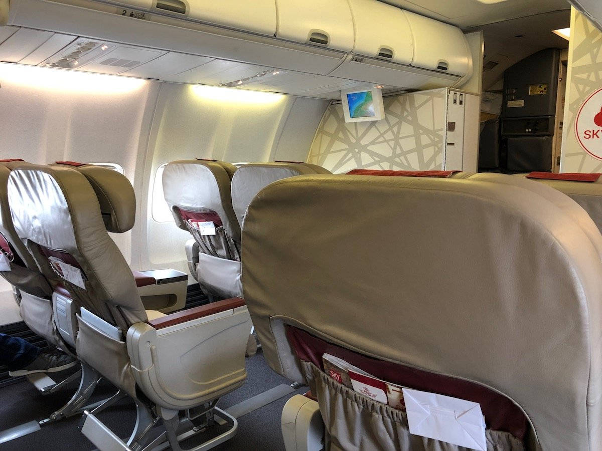 皇家摩洛哥航空飛機內部 壁紙 — 一排排米色飛機座椅，帶有紅色點綴和頭頂行李架，位於光線充足的機艙內部。
