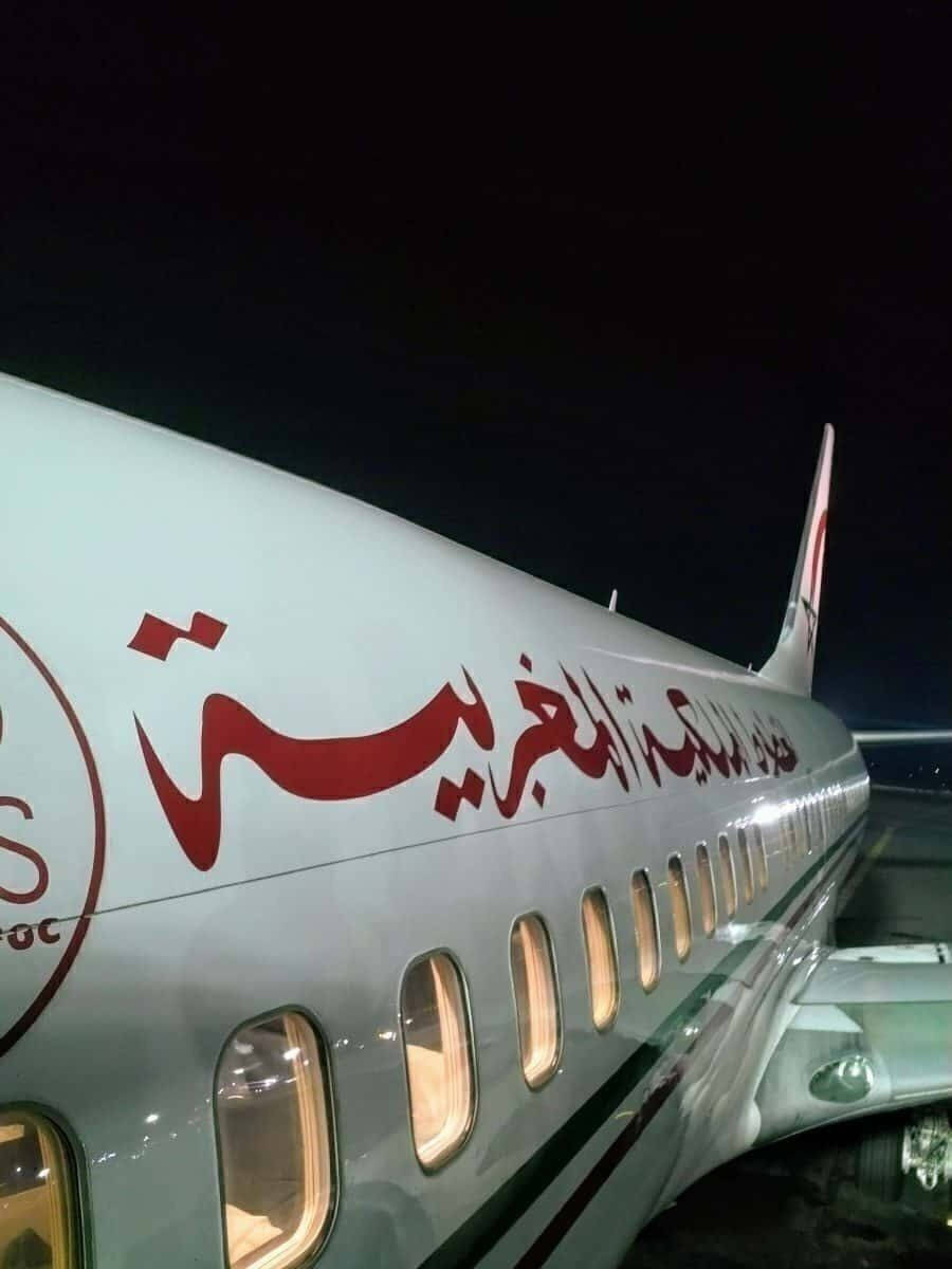 皇家摩洛哥航空飛機窗戶特寫 壁紙 — 一架帶有紅色阿拉伯文字的白色飛機在夜間燈光下閃耀，乘客窗戶從內部照亮。