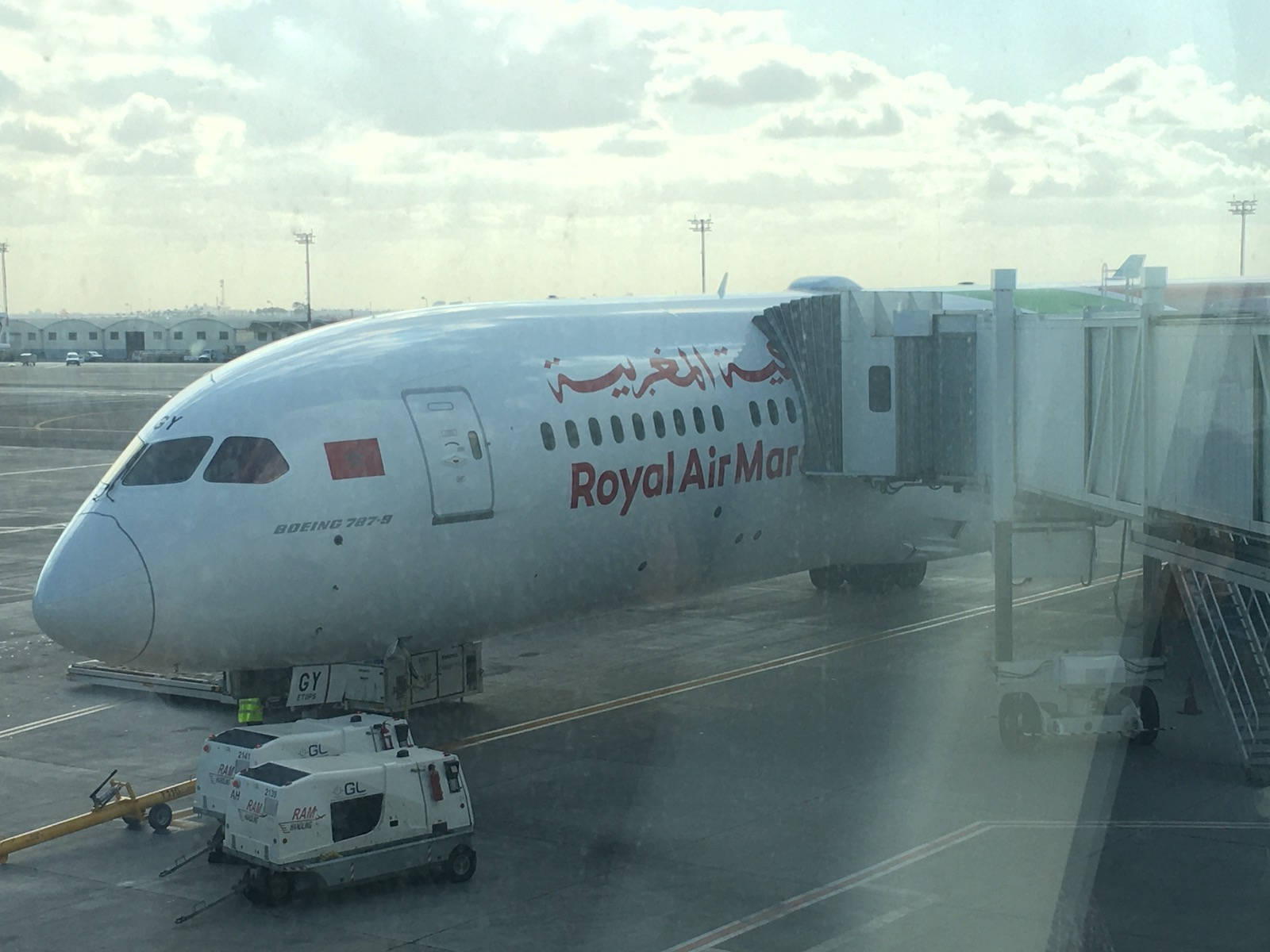 皇家摩洛哥航空飛機與機場車輛 壁紙 — 一架皇家摩洛哥航空波音787停泊在機場閘口，連接了登機橋，天空多雲。