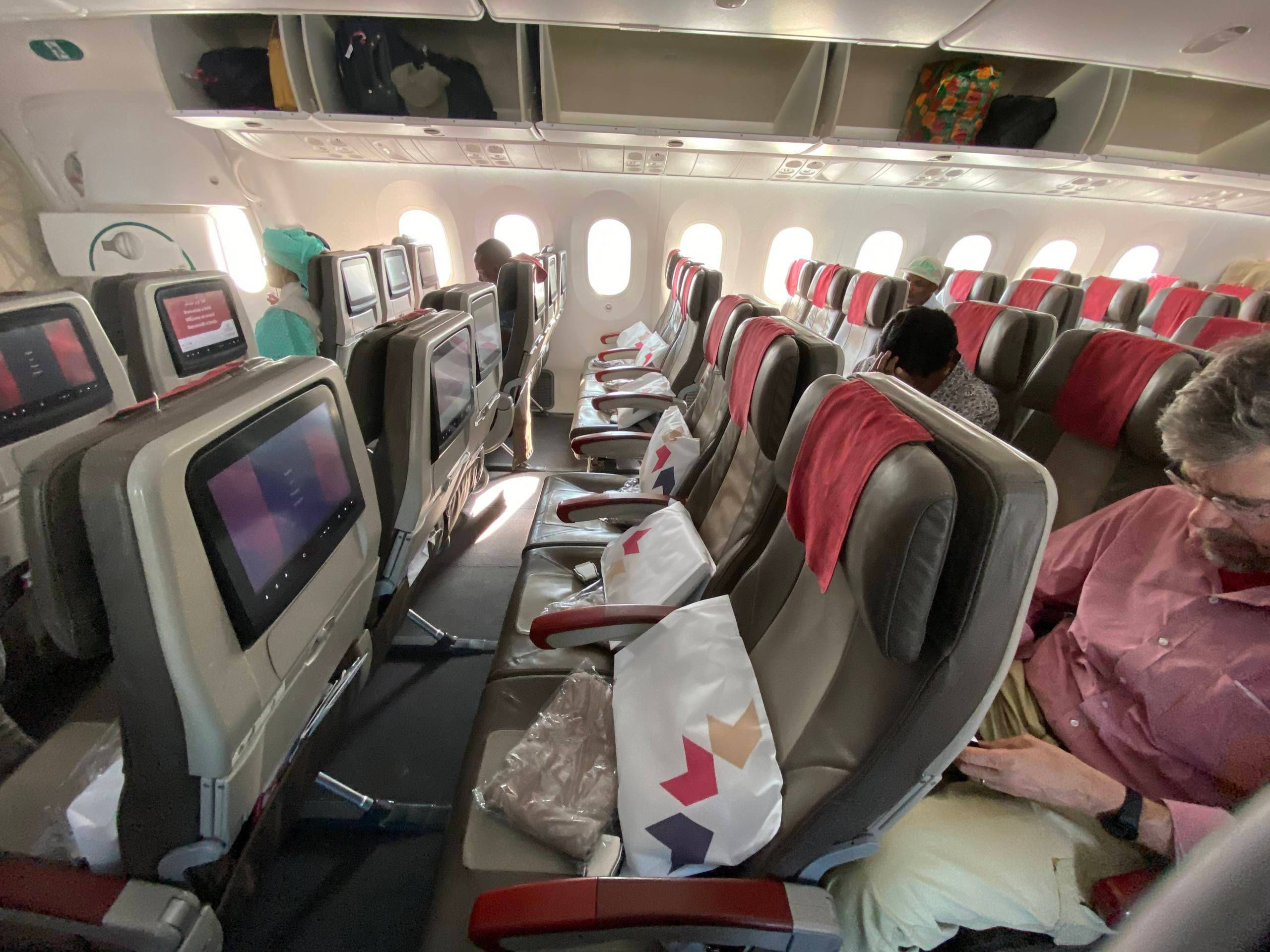 皇家航空馬洛飛機內的舒適座椅 壁紙 — 一排排飛機座位，乘客正在休息，個人屏幕在明亮的機艙中發光。