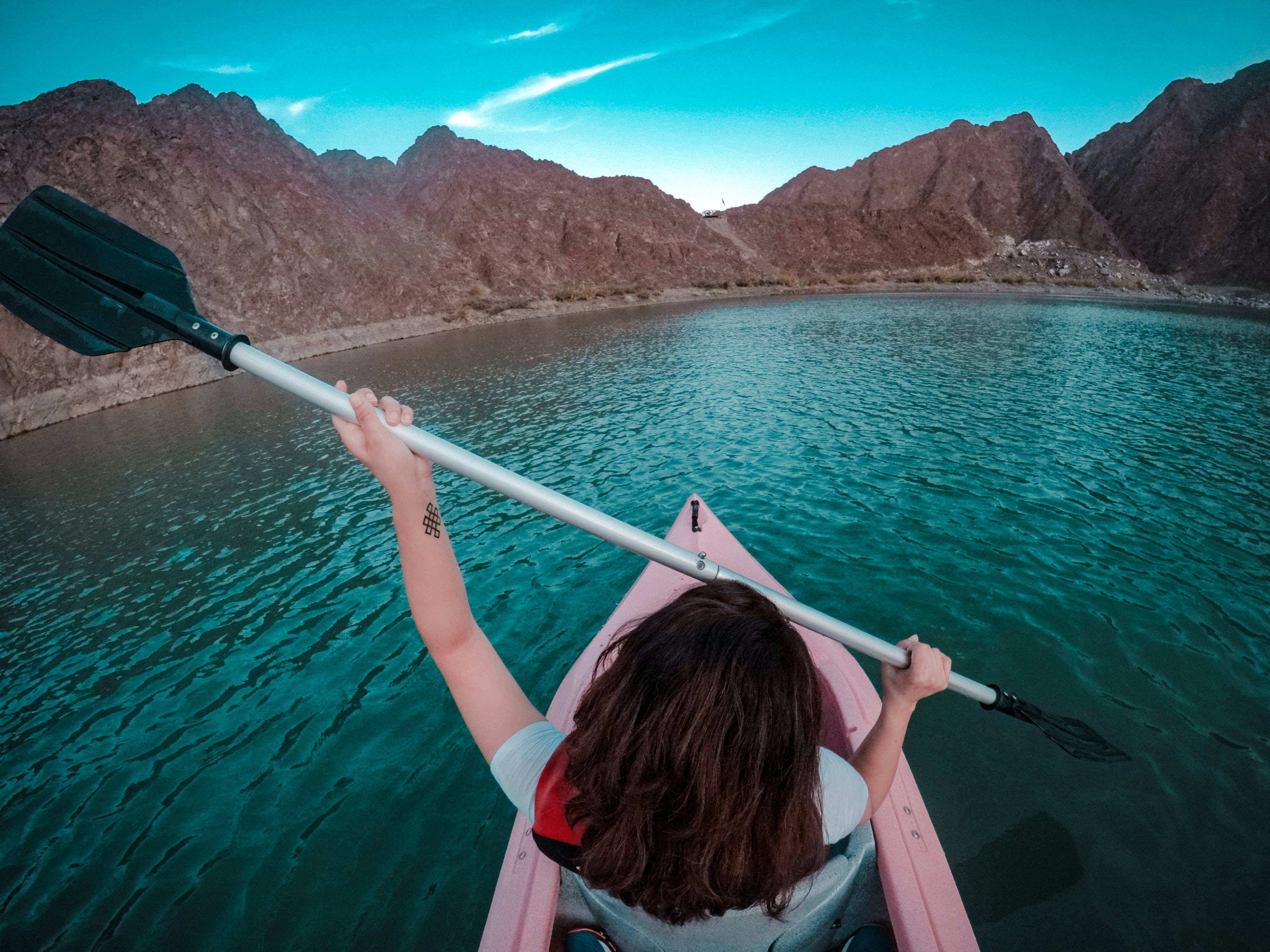 皮划艇者配備 GoPro 壁紙 — 一個人在碧綠色的水上划著粉紅色皮划艇，周圍是崎嶇的棕色山脈，頭頂是清澈的藍天。