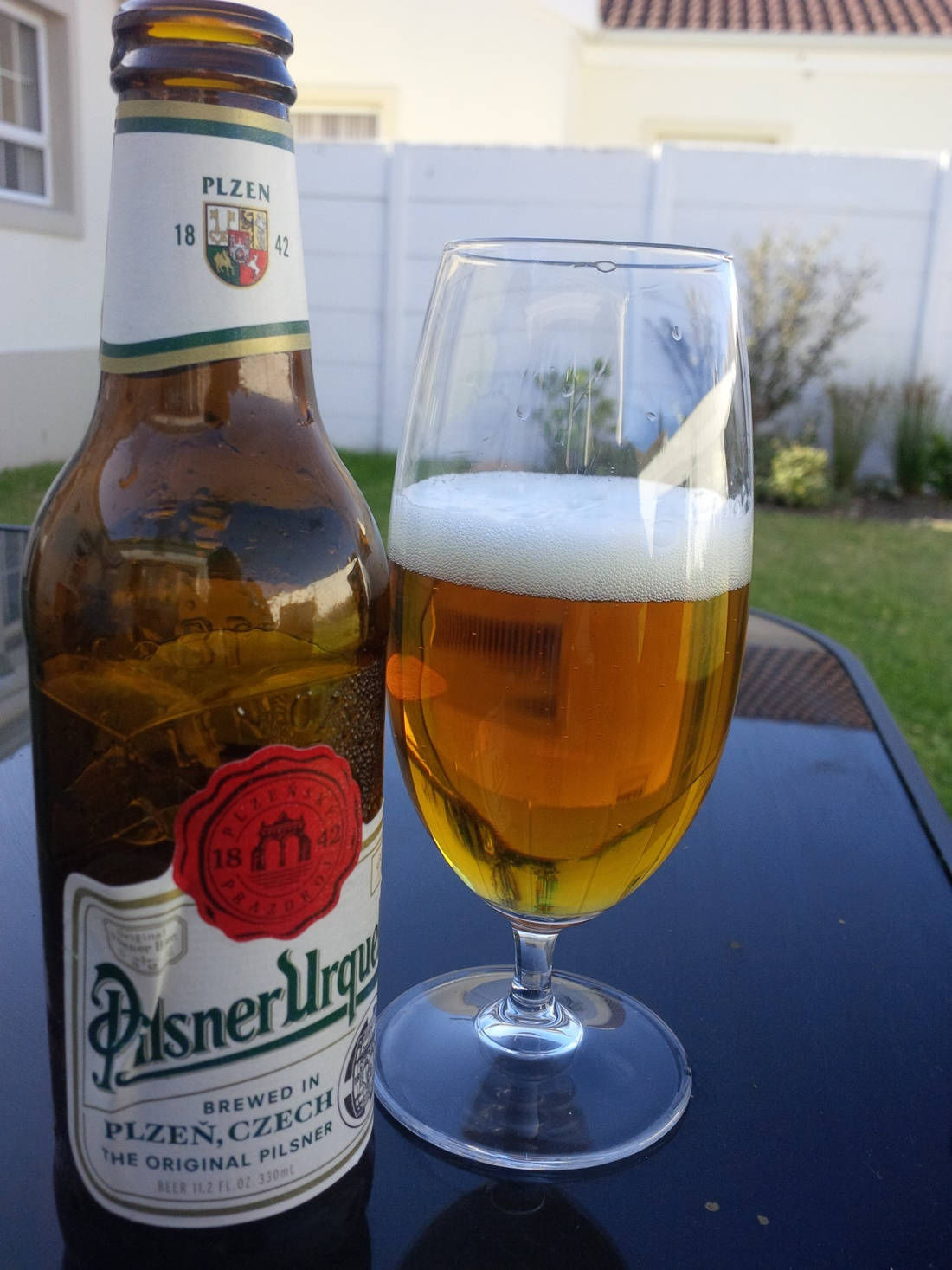 在露台桌子上的一瓶和一杯Pilsner Urquell啤酒。