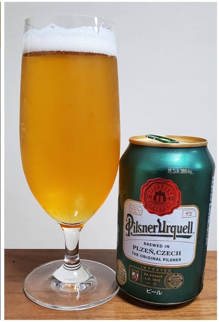一杯啤酒放在木質表面上，旁邊有一個 Pilsner Urquell 罐。