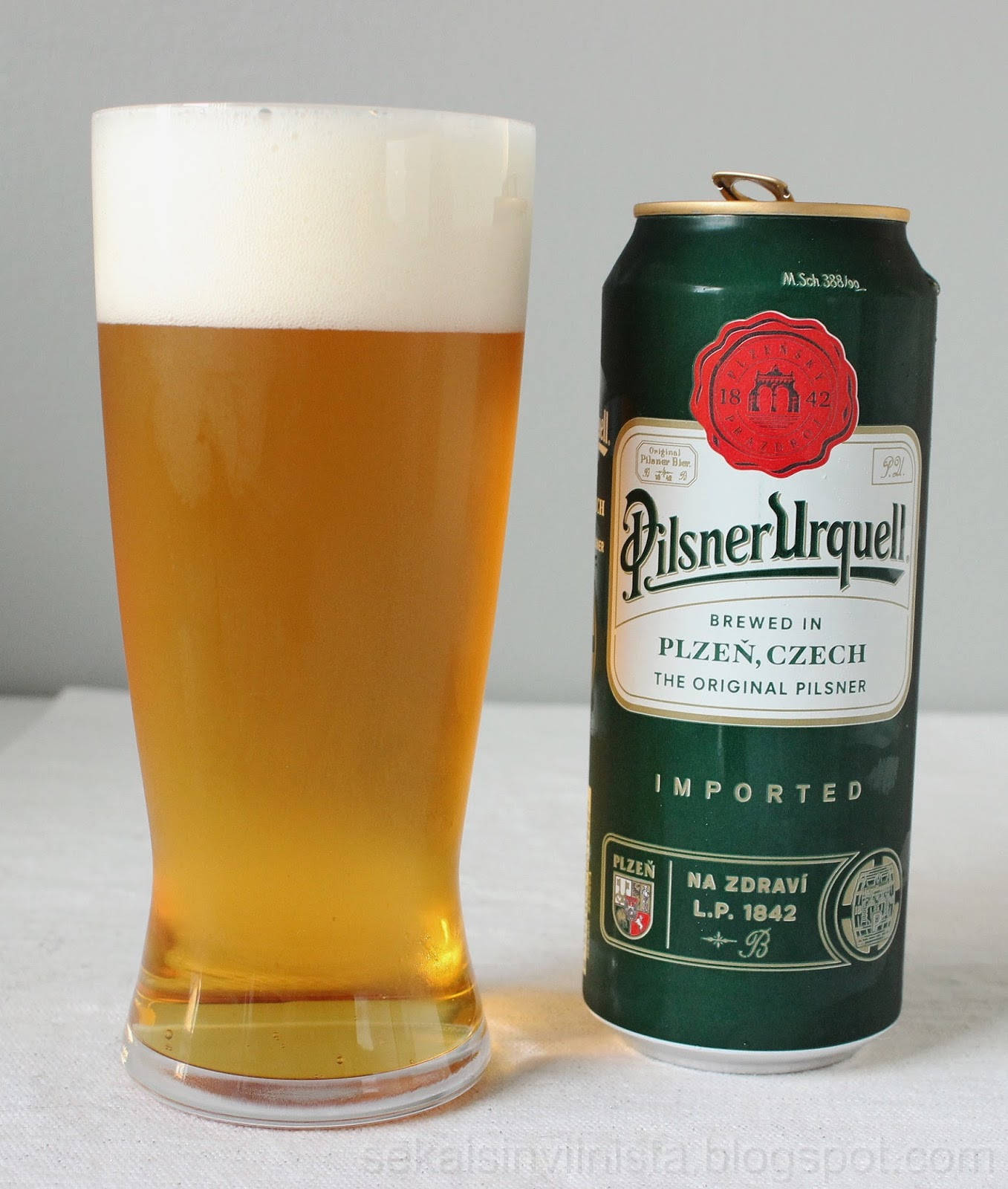 一杯Pilsner Urquell啤酒喺白色表面上面，旁邊係佢嘅綠色罐。