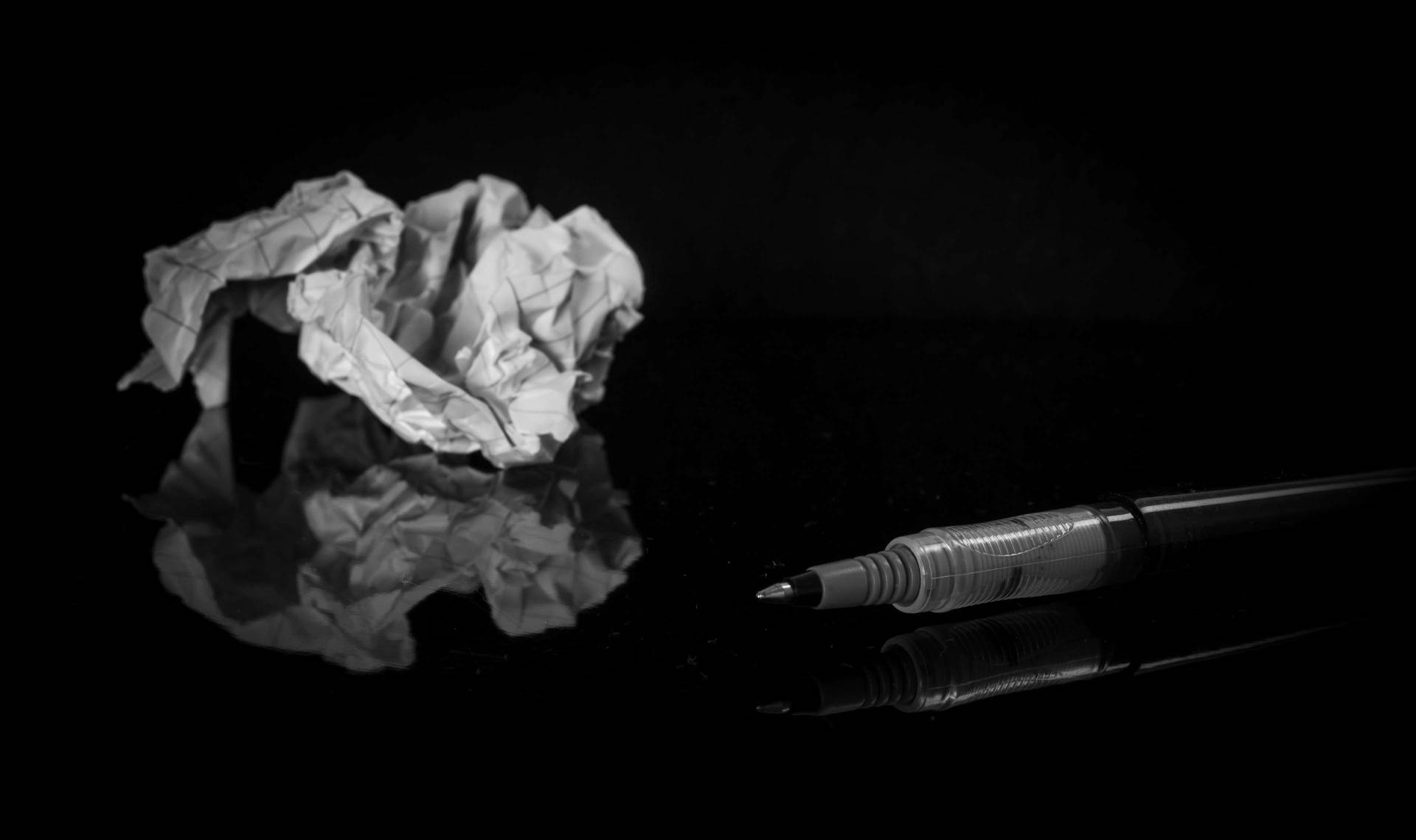 皺巴巴的紙和筆在反射的黑色表面上