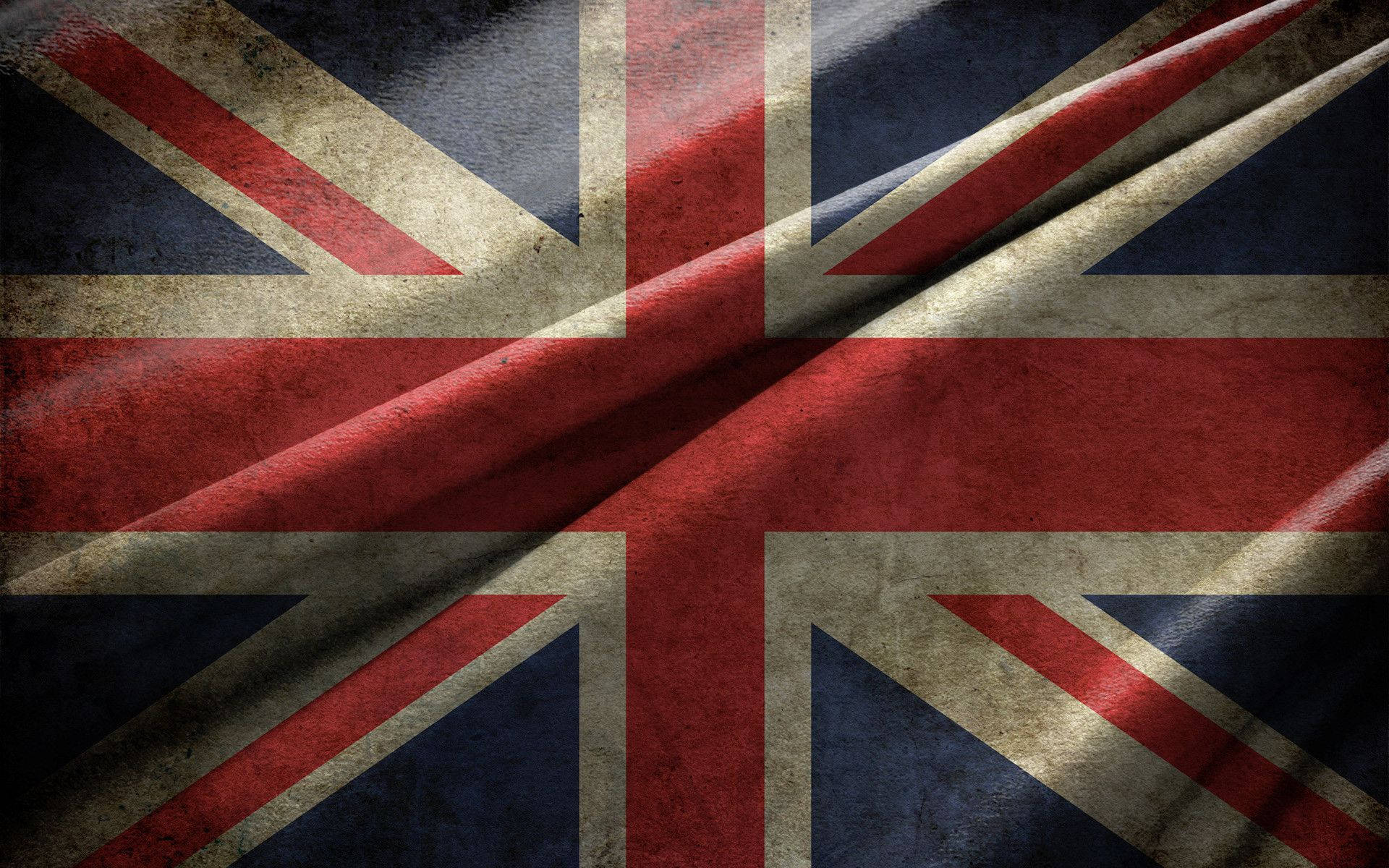 皺褶的英國國旗布料 壁紙 — 一面經風化的英國國旗，帶有深紅、藍色和米白色條紋，在戲劇性的燈光下戲劇性地飄揚。