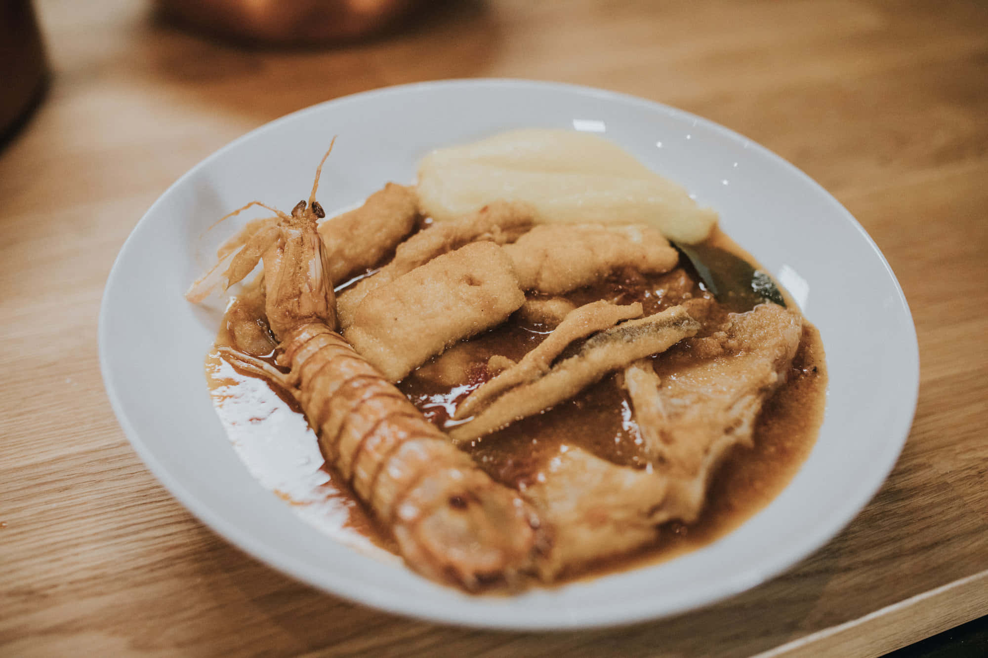 盛裝精美的海鮮布魯德特燉菜 壁紙 — 木桌上白色碟子盛載炸蝦天婦羅和魚塊，配上惹味棕色醬汁的特寫。