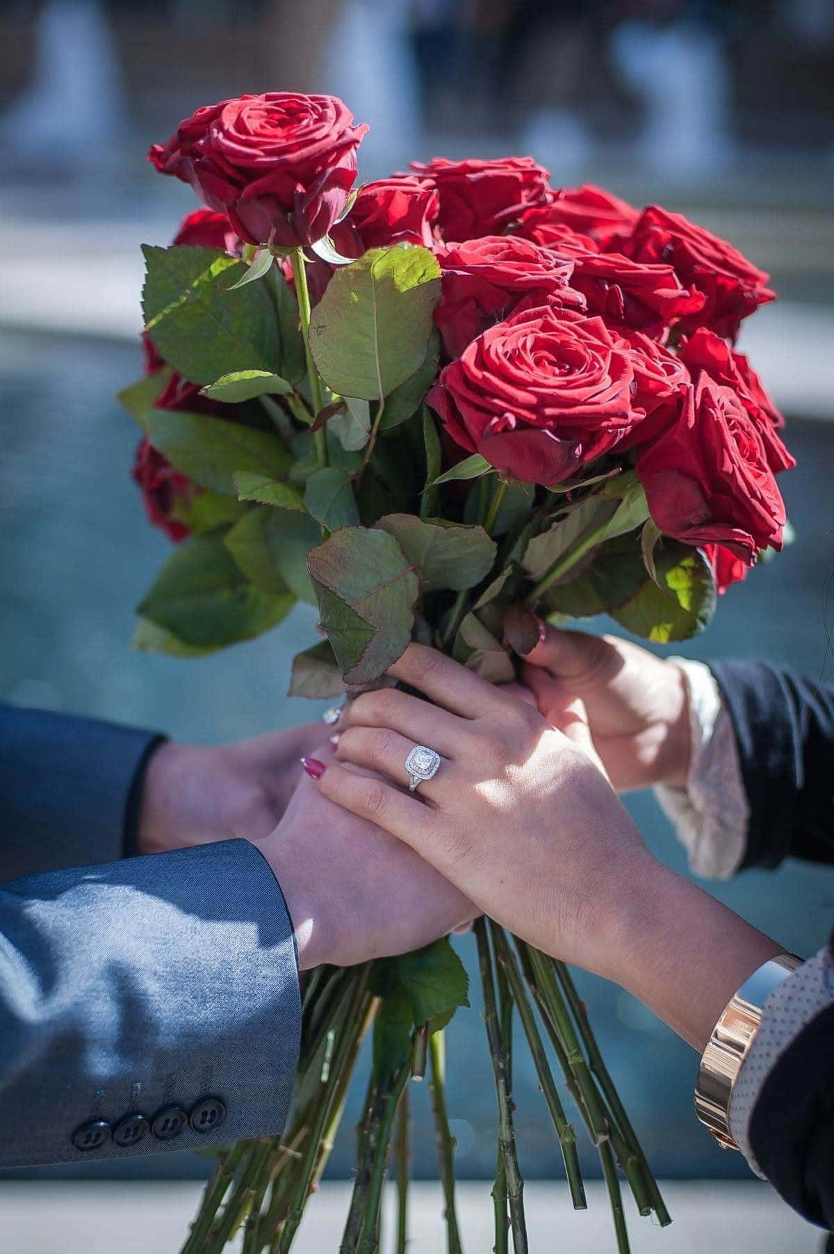 兩隻手緊握一束紅玫瑰，可見結婚戒指。