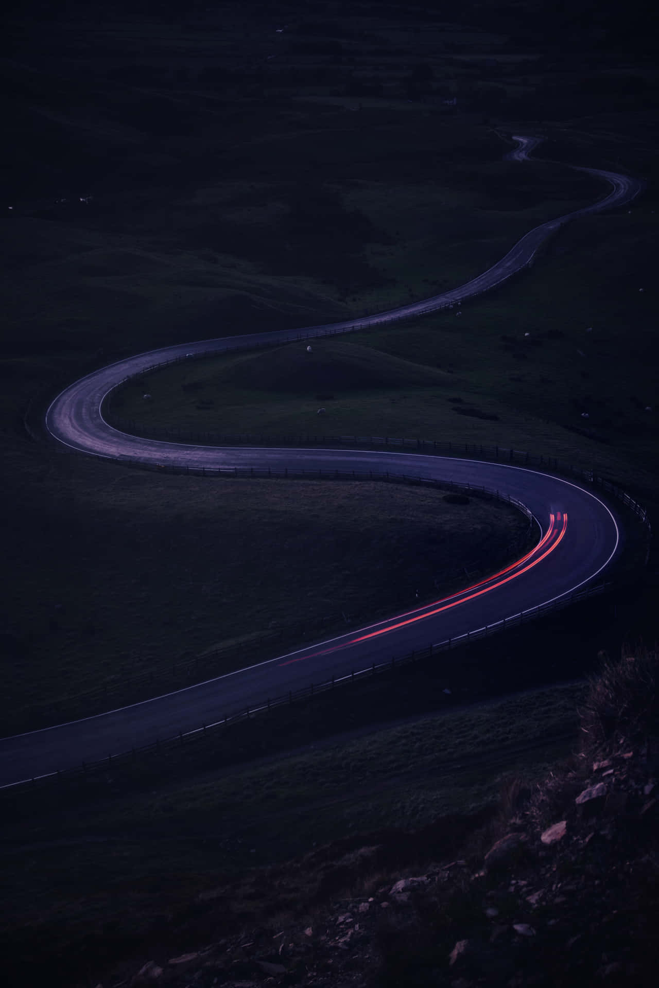 黃昏時分彎曲的道路，行駛車輛留下的紅色光跡。