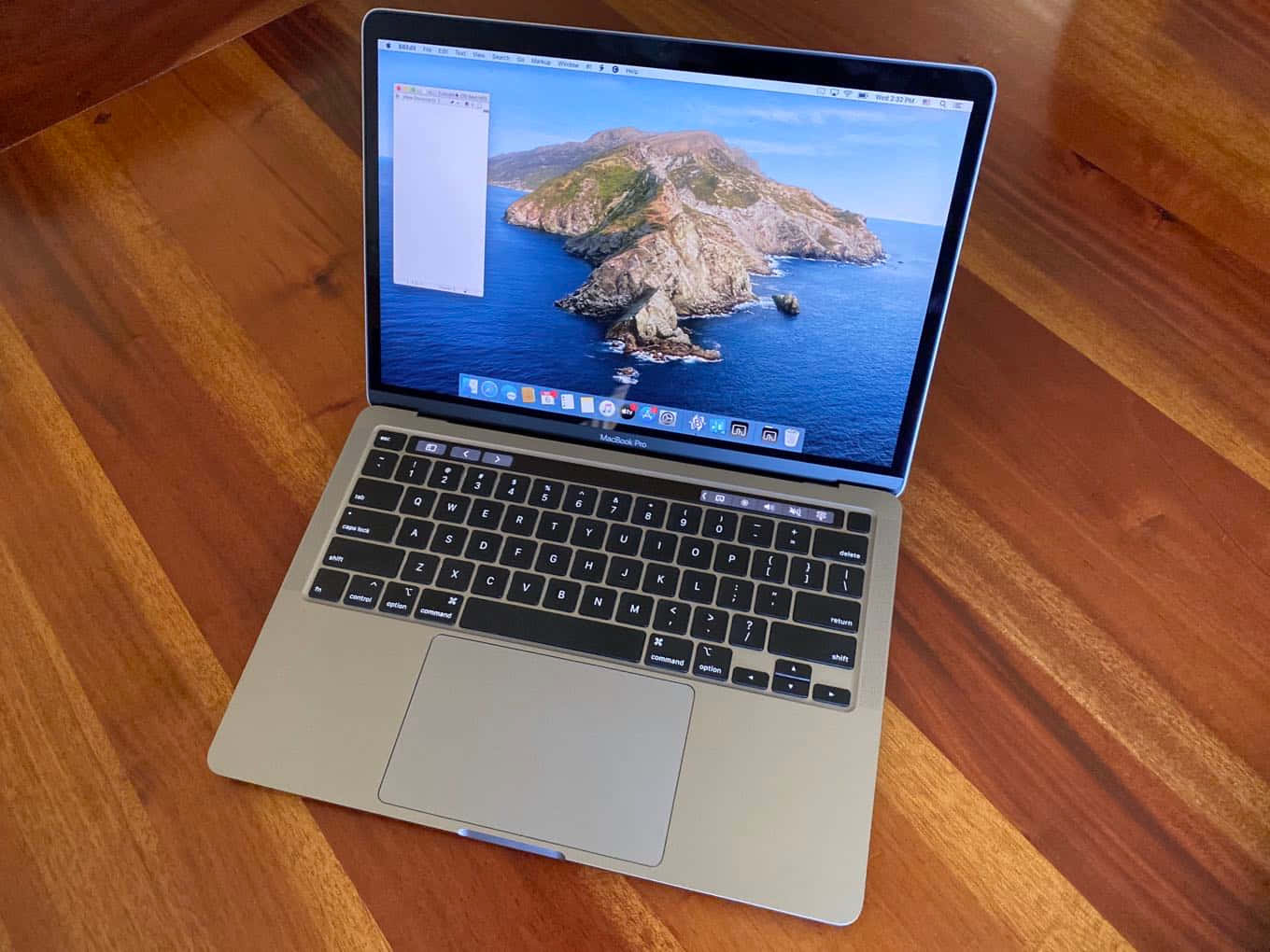 盡享 Macbook 的功能與美學 壁紙 — 銀色手提電腦放在木桌上，顯示藍色海洋中晴朗天空下的岩石島嶼。