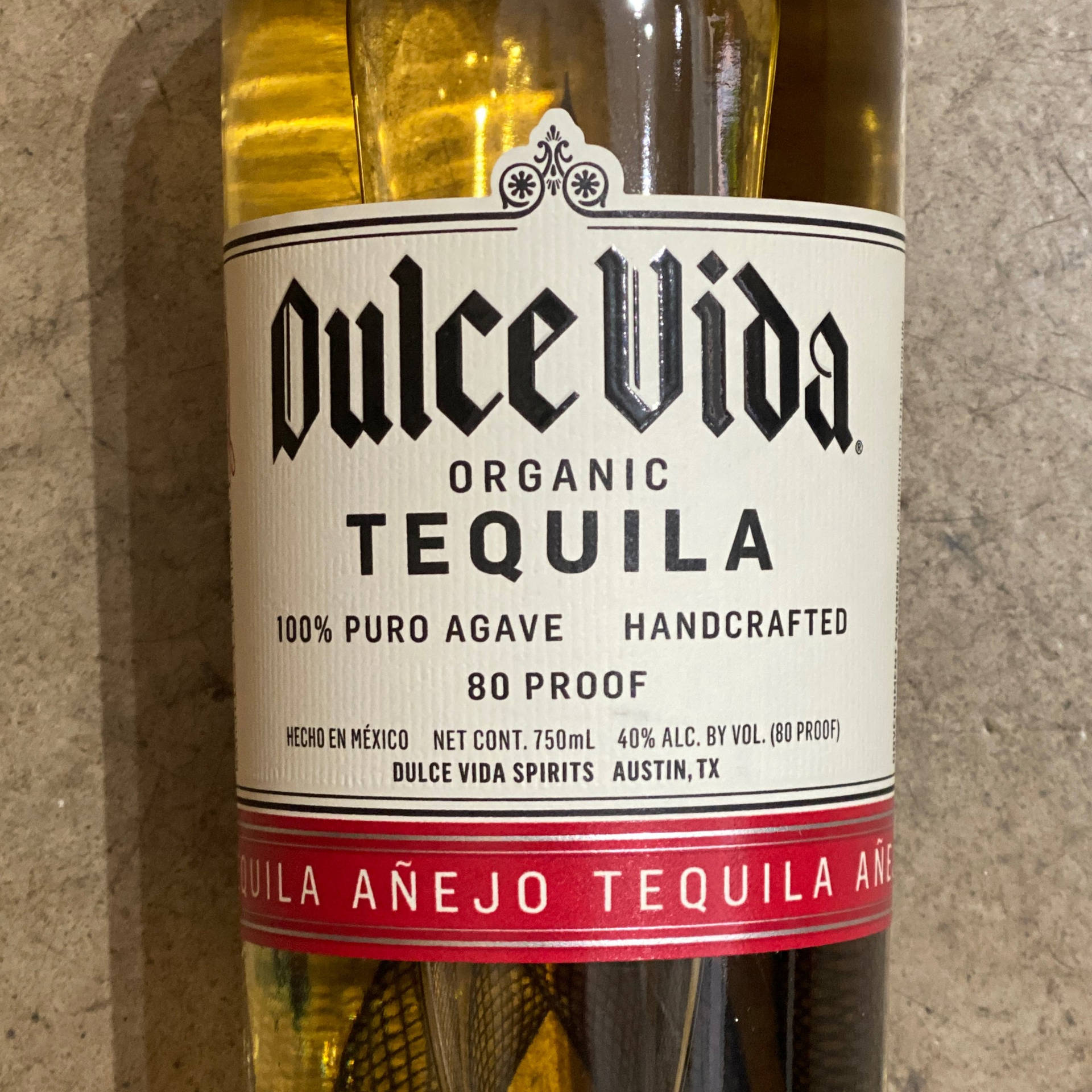 Dulce Vida Organic Tequila 酒瓶標籤，帶有紅色條紋和粗體文字，位於石面上。