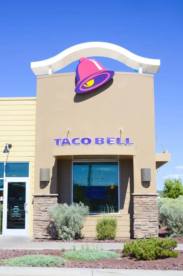 Taco Bell餐廳外觀，帶有粉紅色鐘形標誌和清澈的藍天。