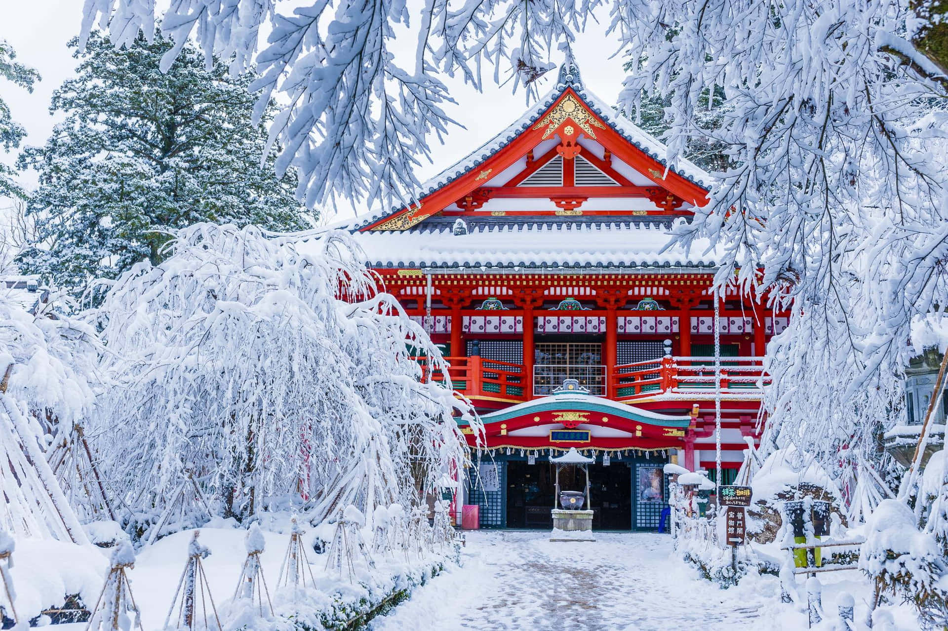 一座被雪覆蓋的紅色日本神社，周圍環繞著霜凍的樹木。
