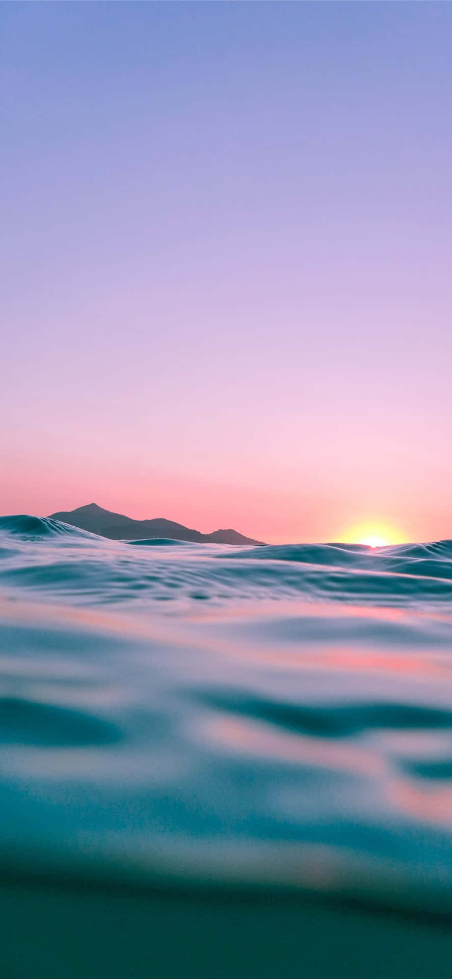 山上的夕陽，平靜的海浪反射粉紅和紫色的天空。