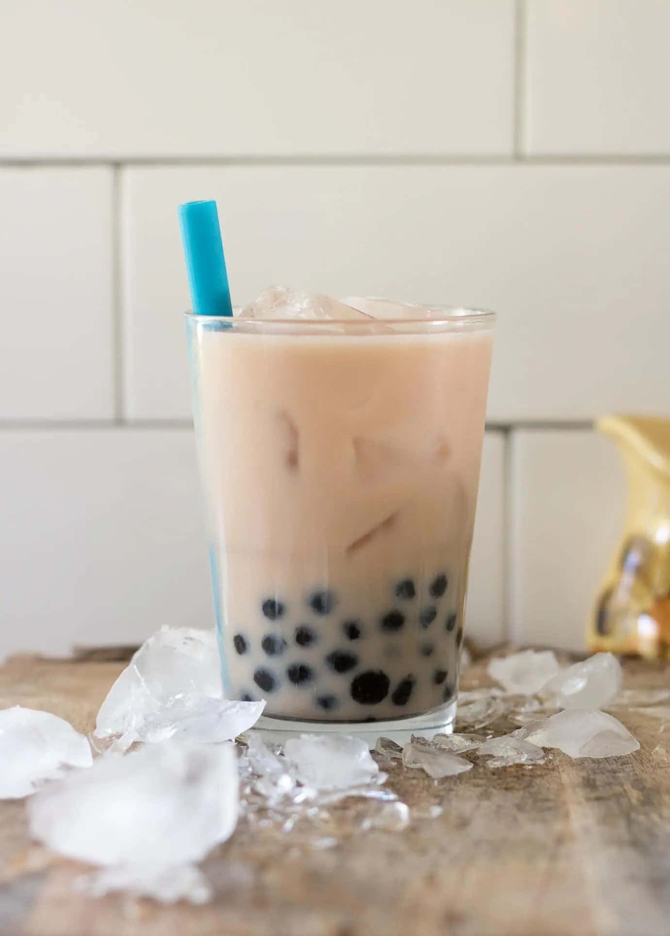 「盡情享受最美味的珍珠奶茶！」 壁紙 — 一杯高身嘅忌廉冰凍珍珠奶茶，有黑色珍珠同藍色飲管，放喺木質表面上，周圍有融化緊嘅冰塊。