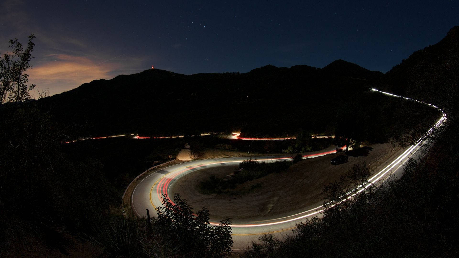 暮色中的山路，在星空下閃爍著車燈軌跡。