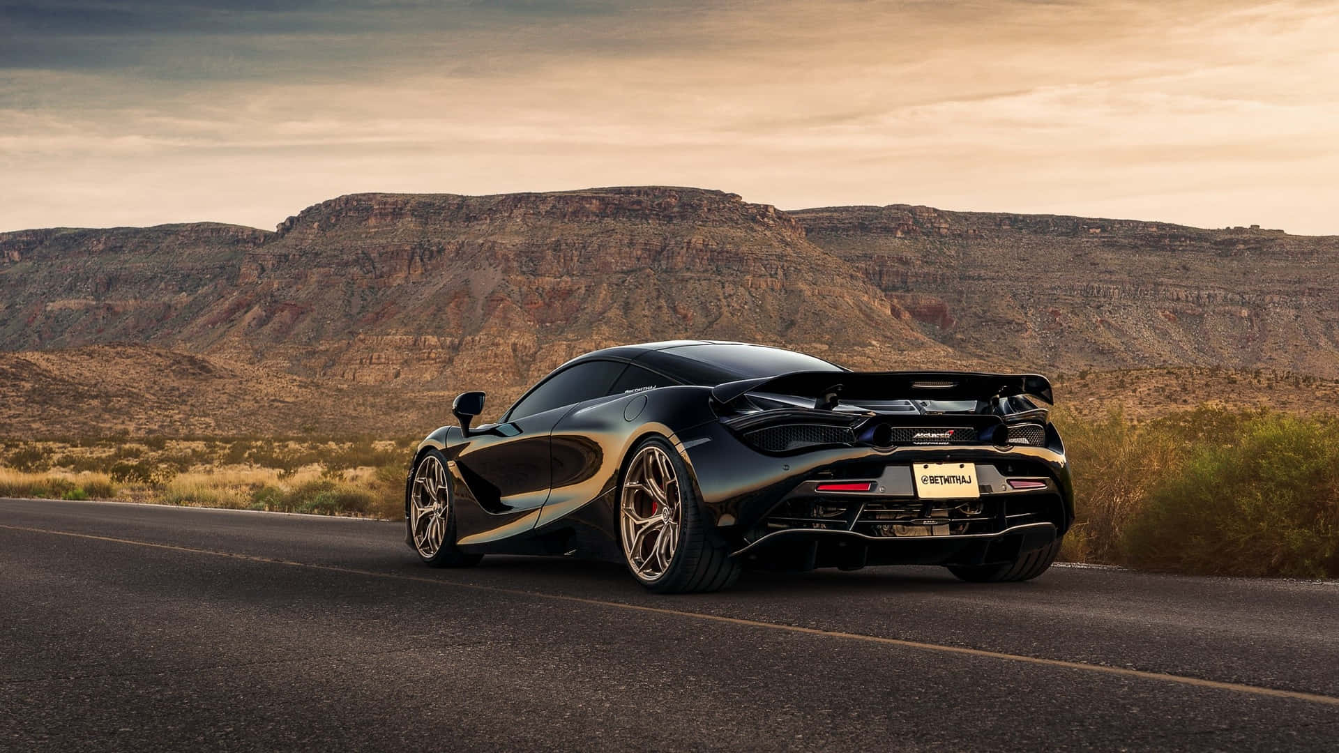 黑色McLaren跑車在日落時分行駛在沙漠道路上