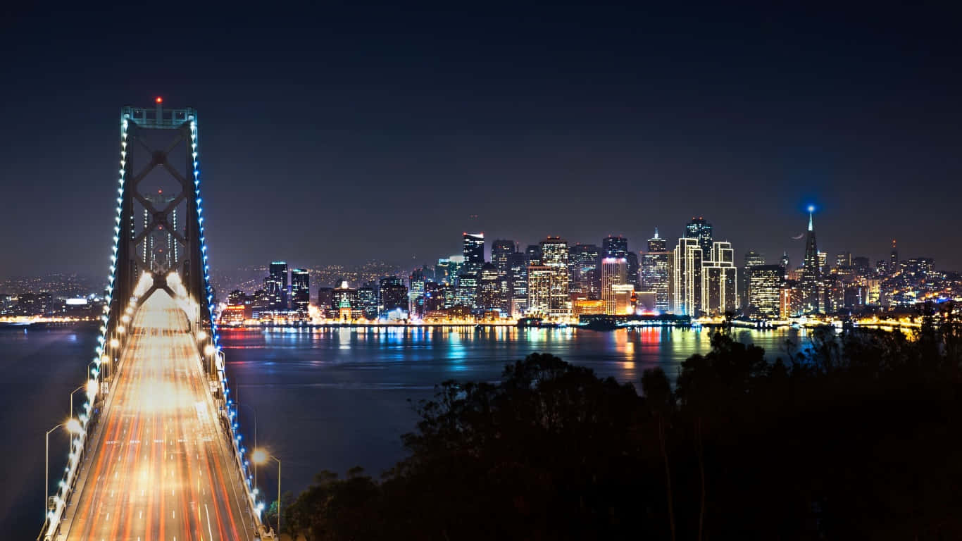 夜間城市景觀，包括燈火通明的灣區大橋和舊金山天際線，水面上的光跡。