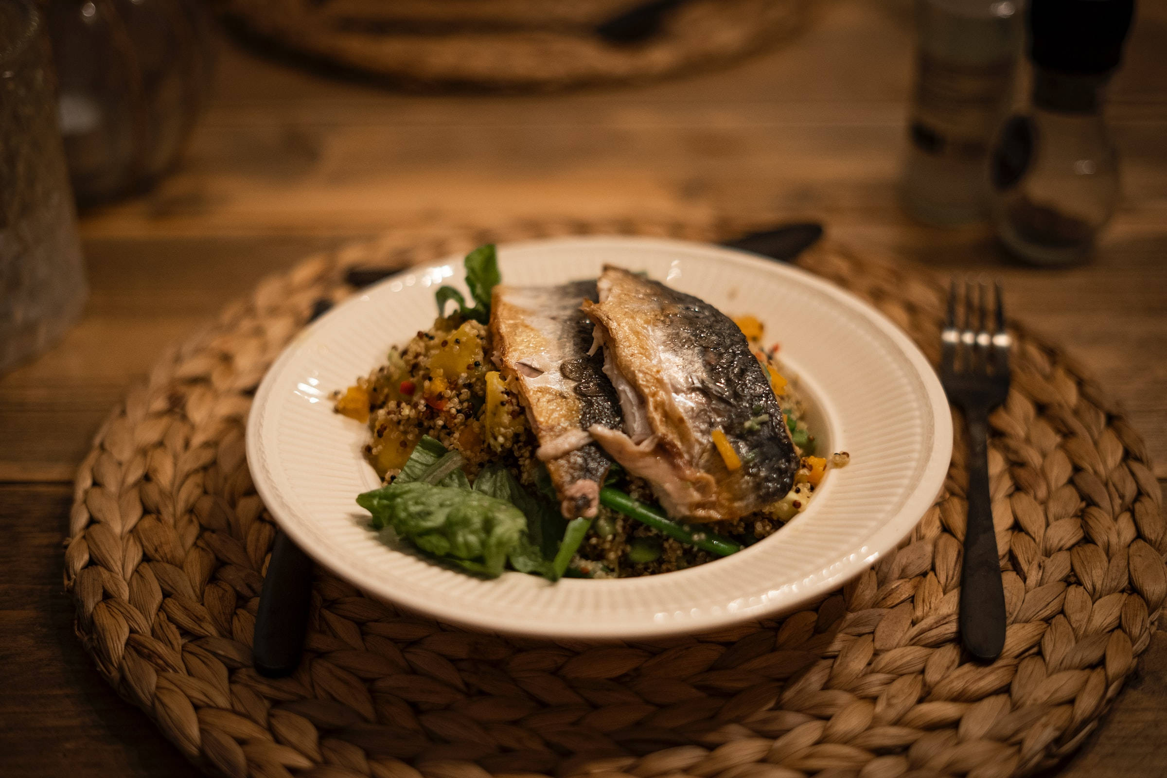 盤中新鮮鰹魚沙拉 壁紙 — 一盤烤魚配藜麥和青菜，溫暖地照亮在木桌上編織的餐墊上。
