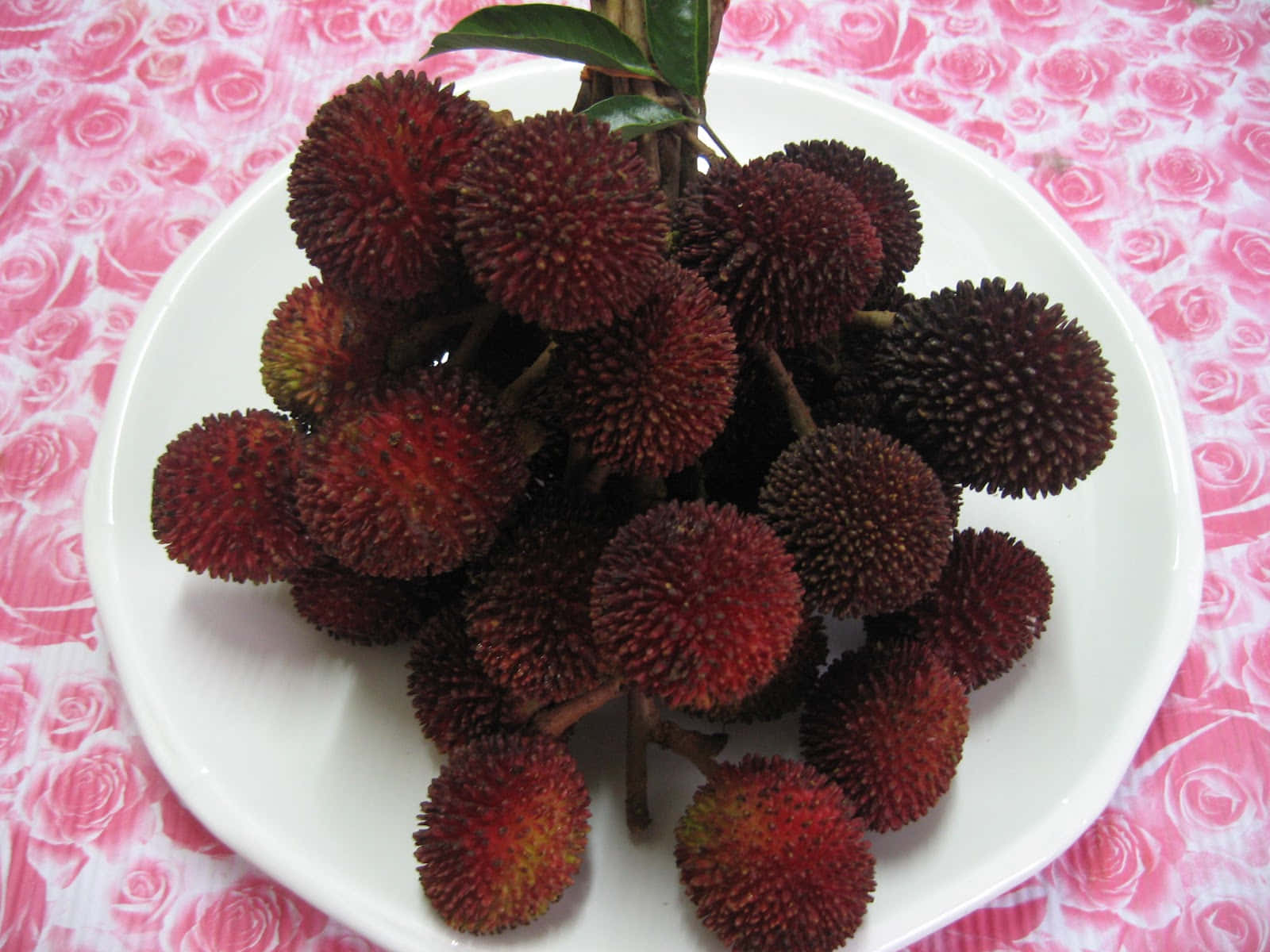 一碟新鮮紅色荔枝配綠葉，放在粉紅色玫瑰枱布上。