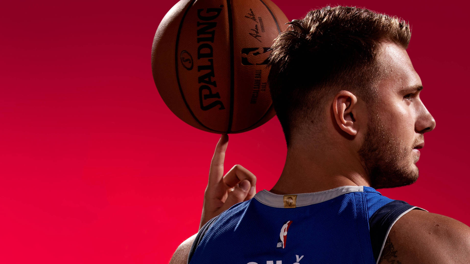盧卡·東契奇 NBA 桌面壁紙 壁紙 — 一名籃球運動員在鮮紅色背景前用指尖平衡 Spalding 球。