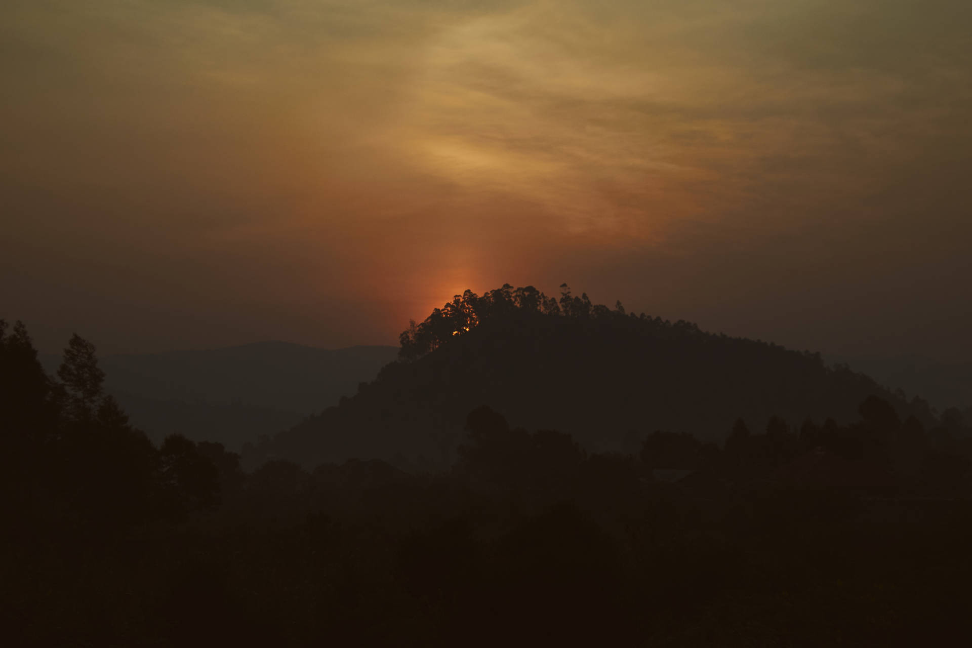 夕陽在森林覆蓋的山丘後方，在朦朧的山谷中投射出剪影。