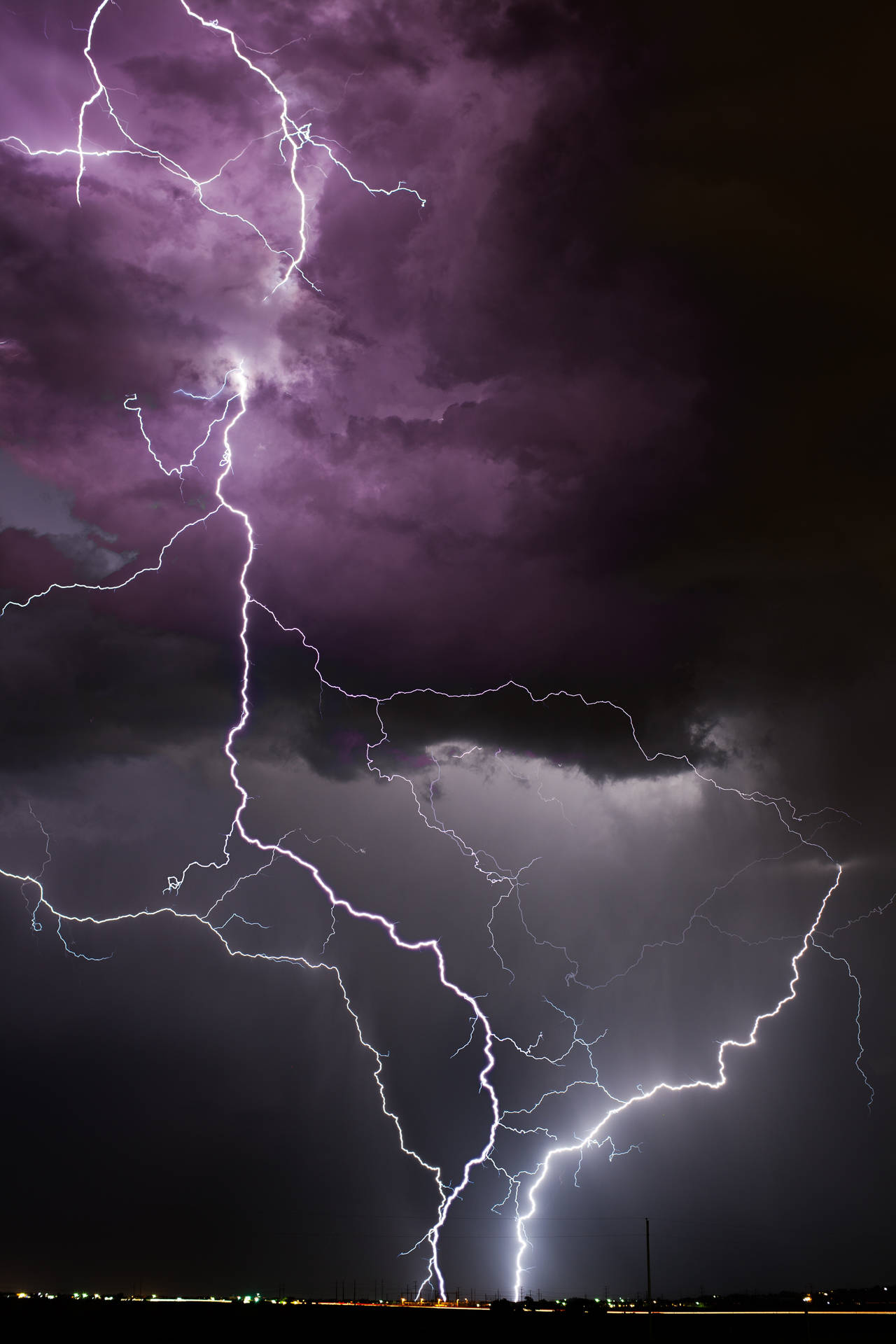 強烈的閃電在遠處城市上空的暴風雨紫色夜空中劈啪作響。