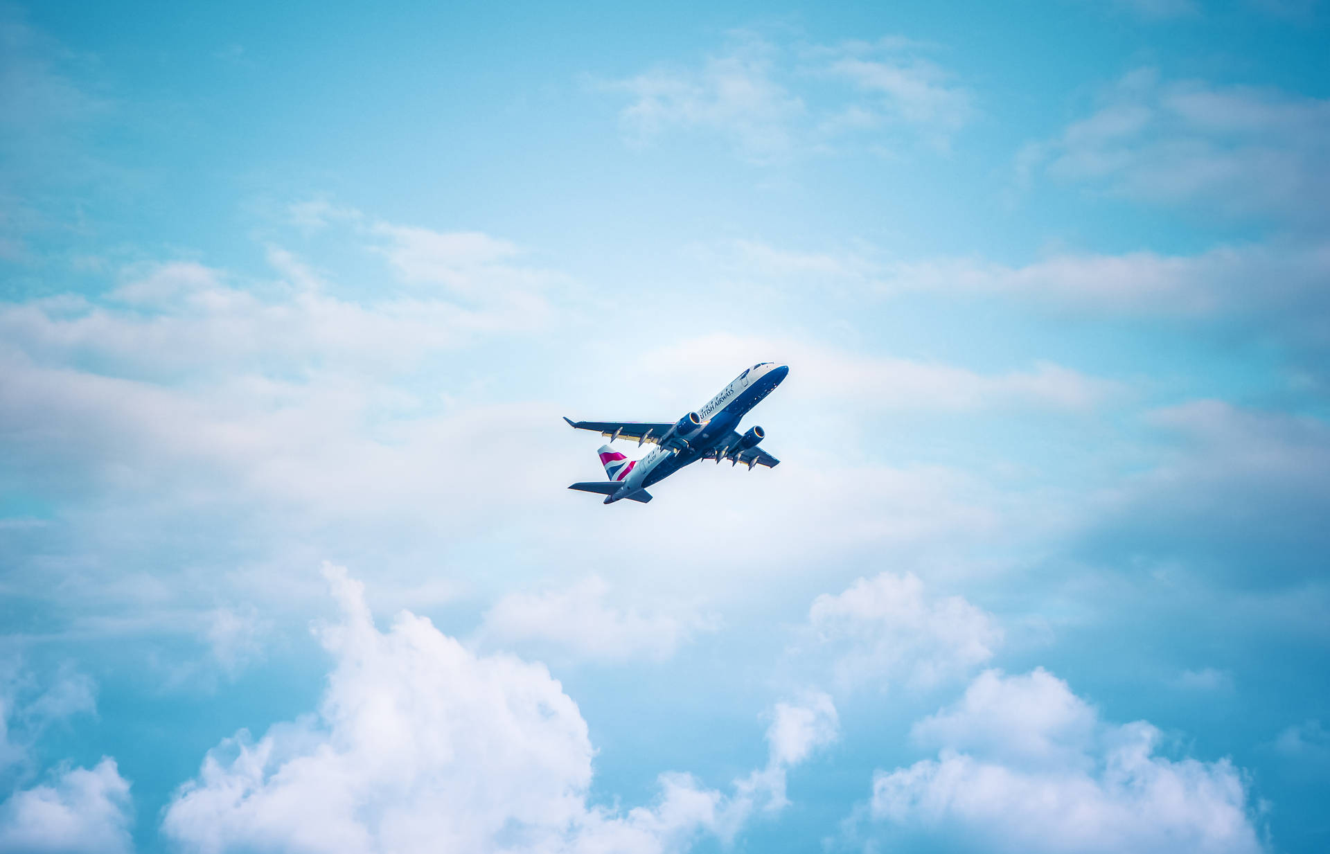 一架英國航空公司的飛機在清澈的藍天中，高高飛過蓬鬆的白雲。