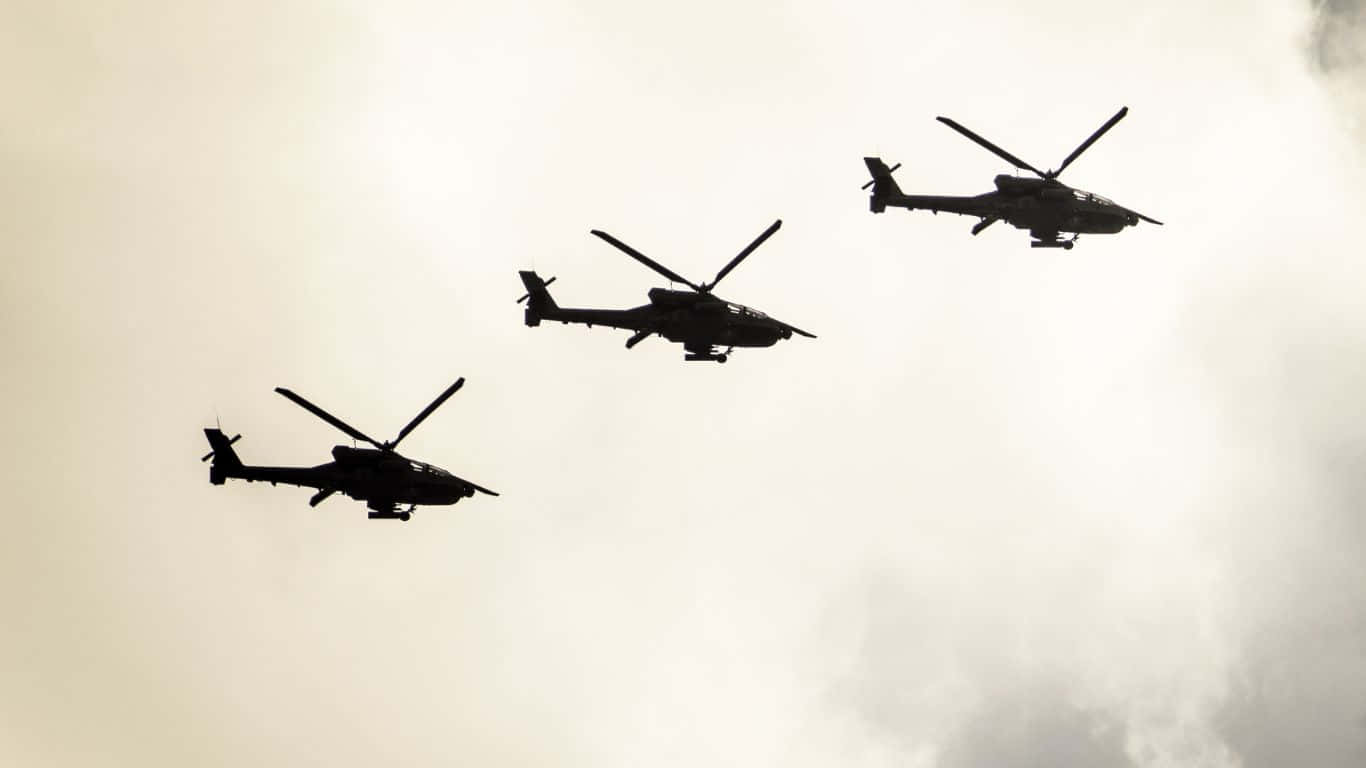直升機群翱翔天際 壁紙 — 三架軍用直升機以黑色剪影形式編隊飛行，背景是明亮的陰天。